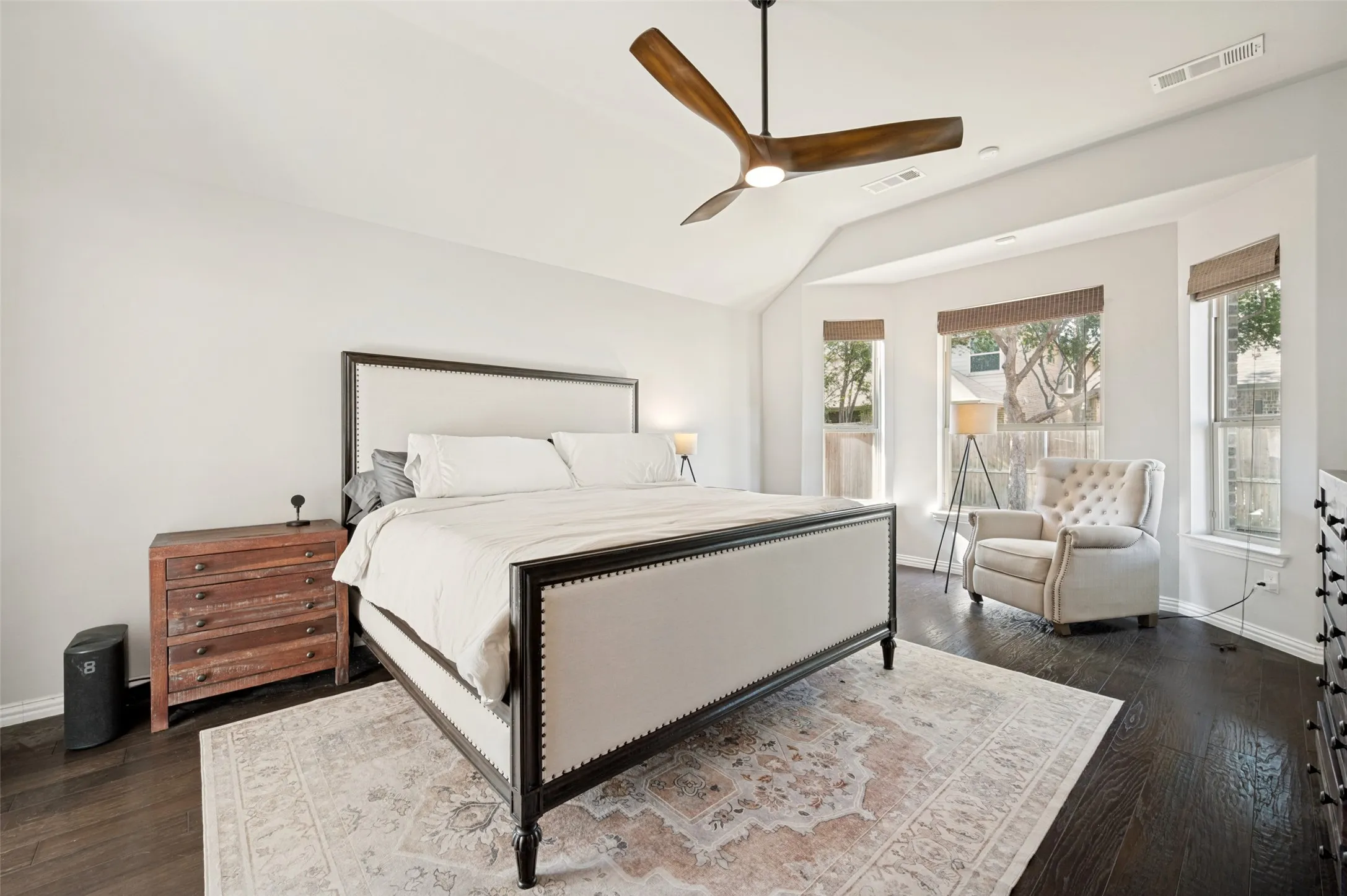 Bedroom featuring dark wood-finish flooring, a contemporary ceiling fan, and a bay window configuration with three windows and woven shades