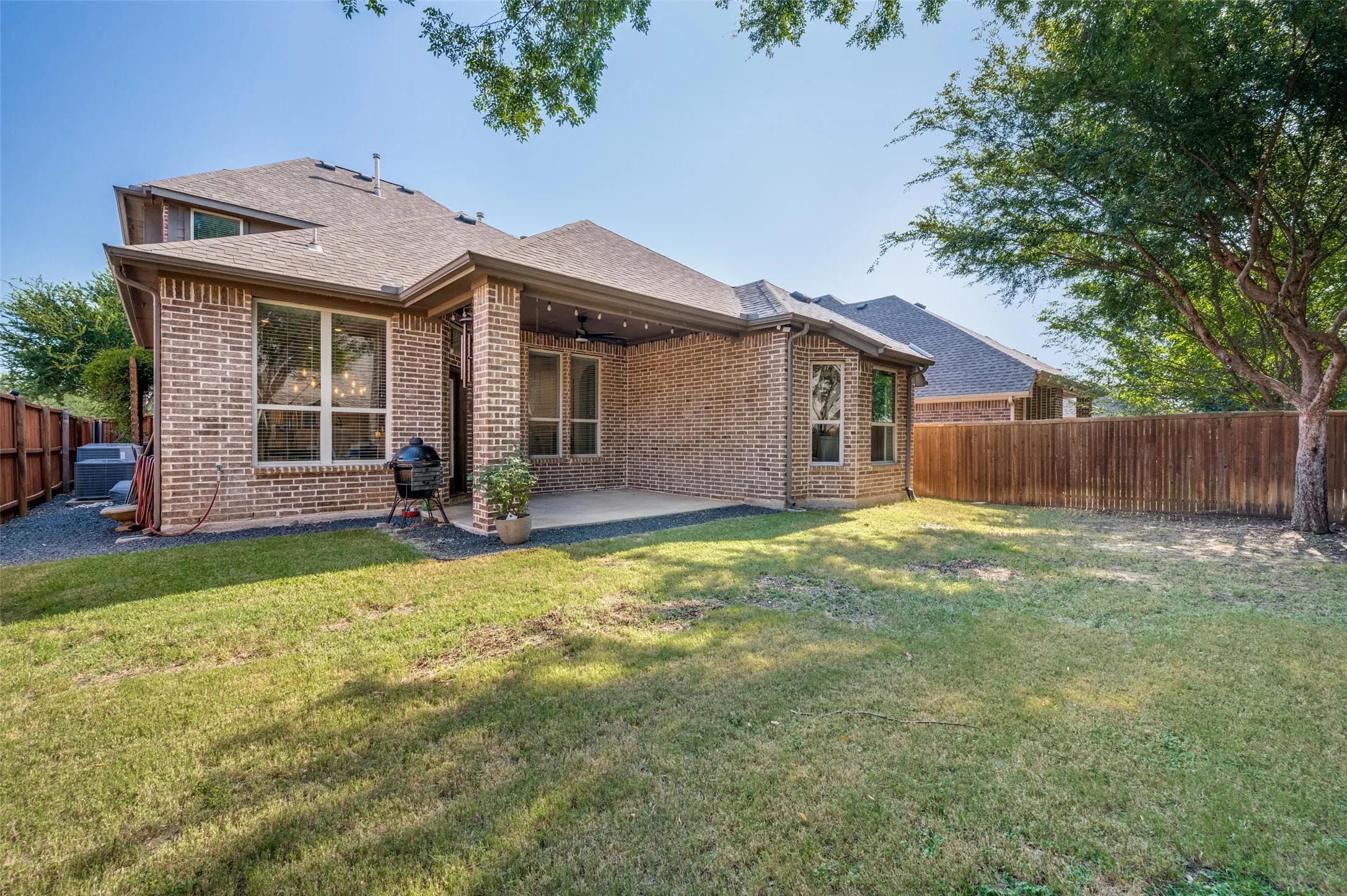 Expansive backyard featuring a brick exterior with multiple windows, a covered patio with recessed lighting, and a full privacy fence