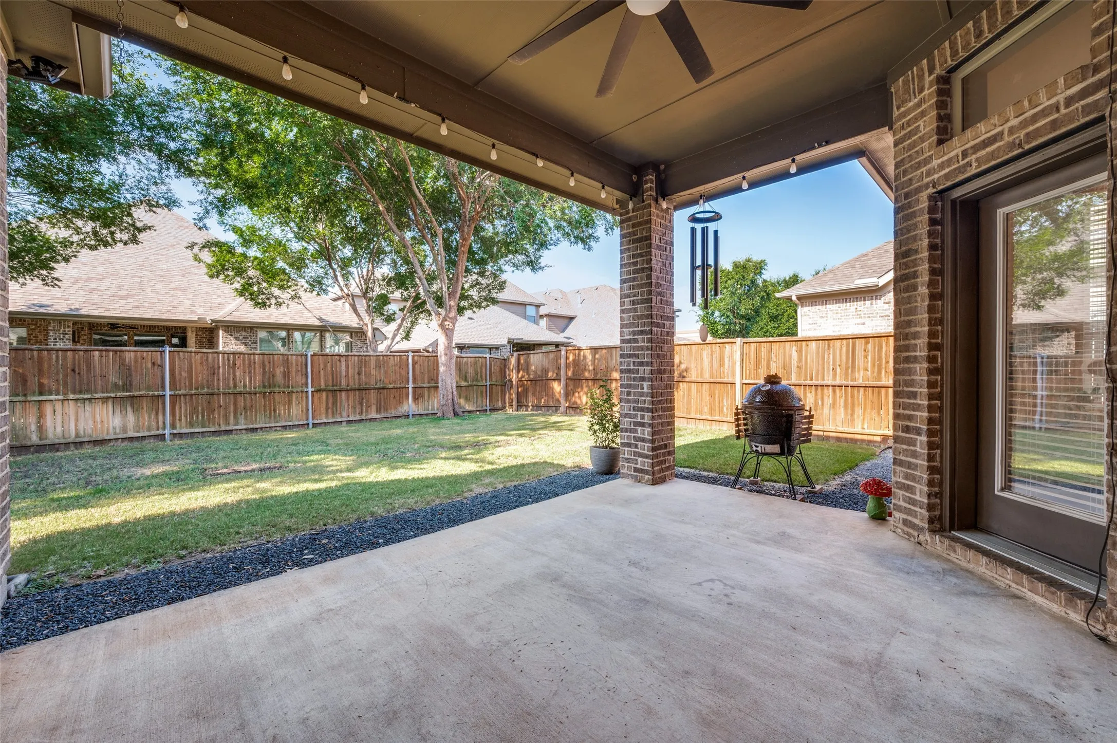 Covered concrete patio with a ceiling fan, string lighting, and brick columns