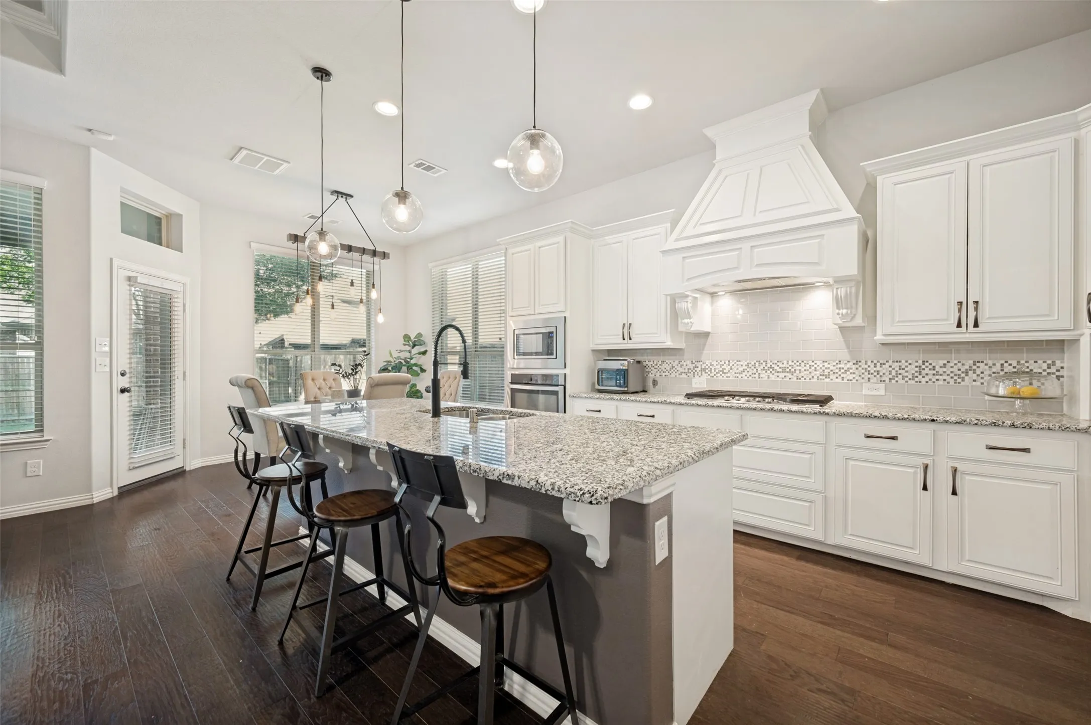 Gourmet kitchen featuring a large island with seating, granite countertops, white cabinetry, a decorative range hood, and dark wood-finish flooring