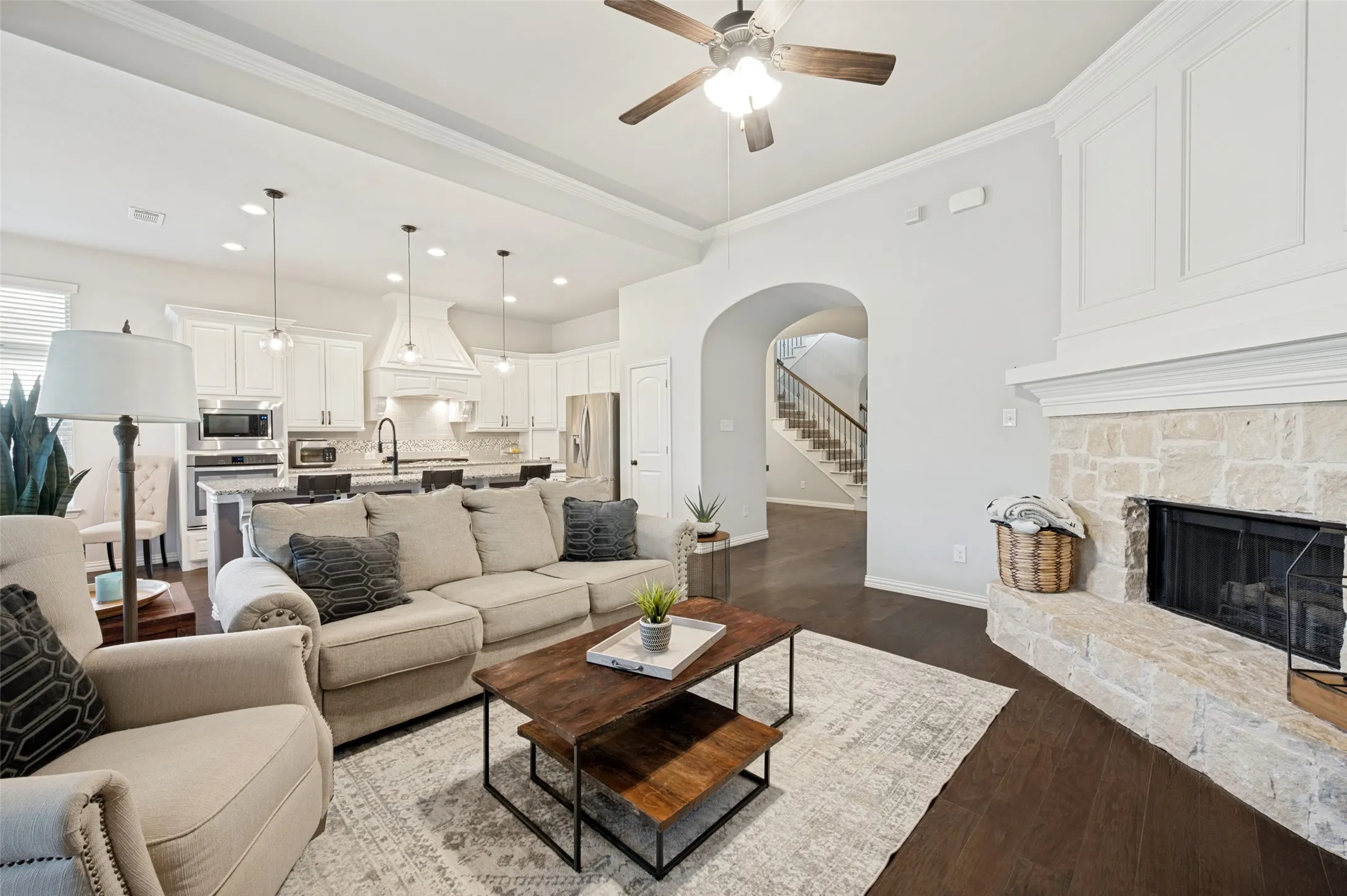 Living area featuring dark wood-finish flooring, a stone fireplace with a white mantel, and an arched entryway leading to a staircase