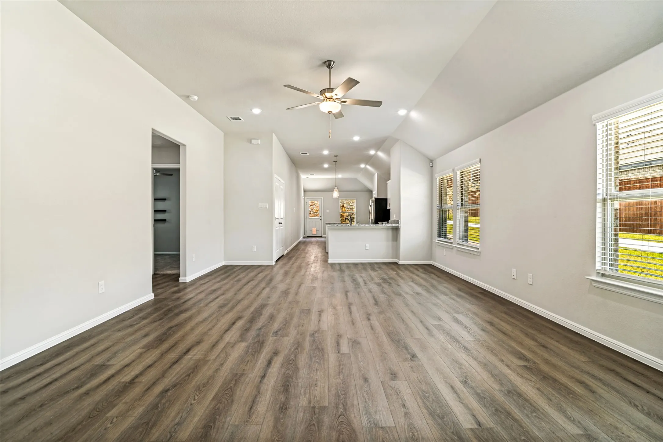 Spacious living area featuring wood-finish flooring, vaulted ceilings, and recessed lighting