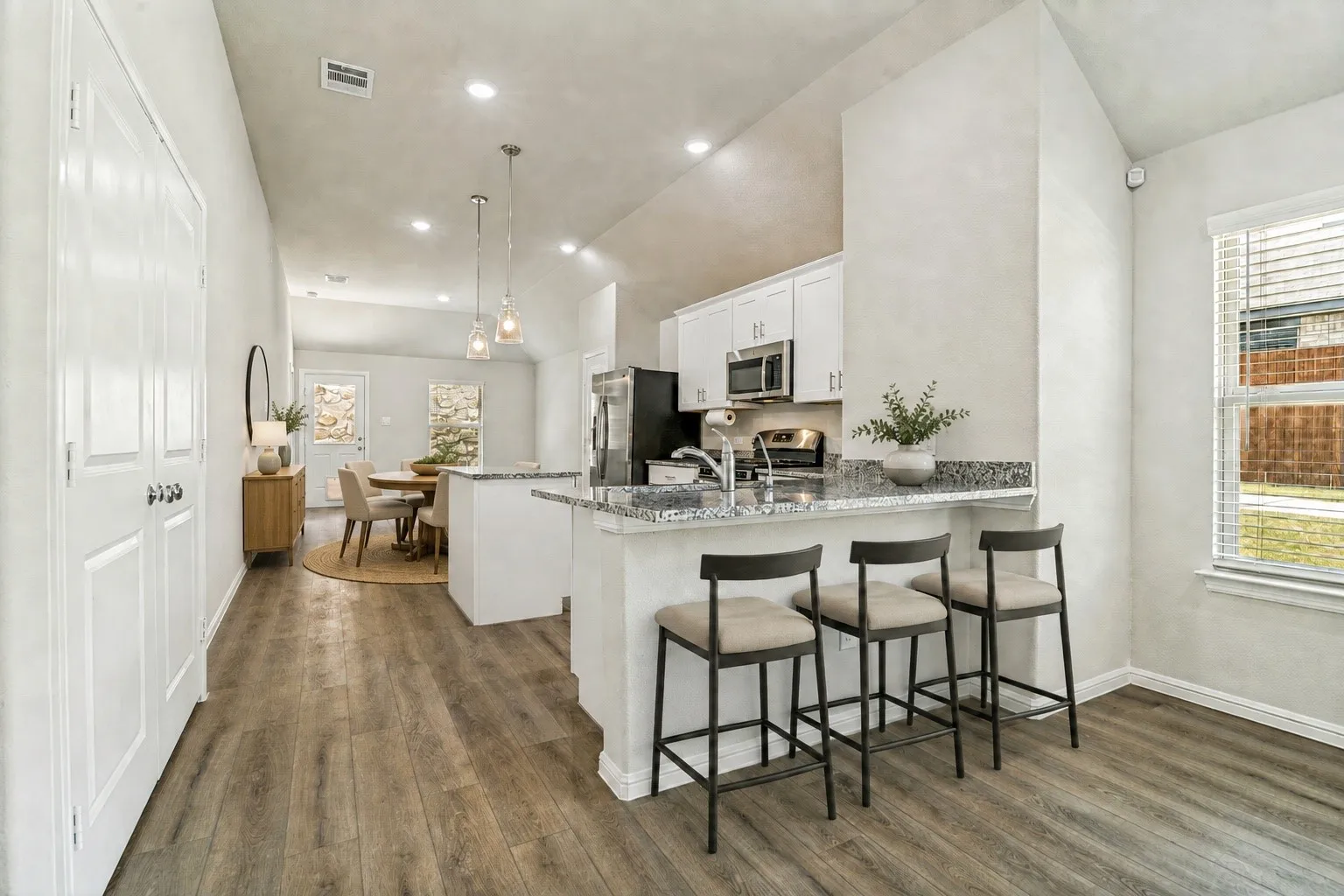 Vaulted ceiling, recessed lighting, wood-finish flooring, white cabinetry, and stainless steel appliances (virtually staged)