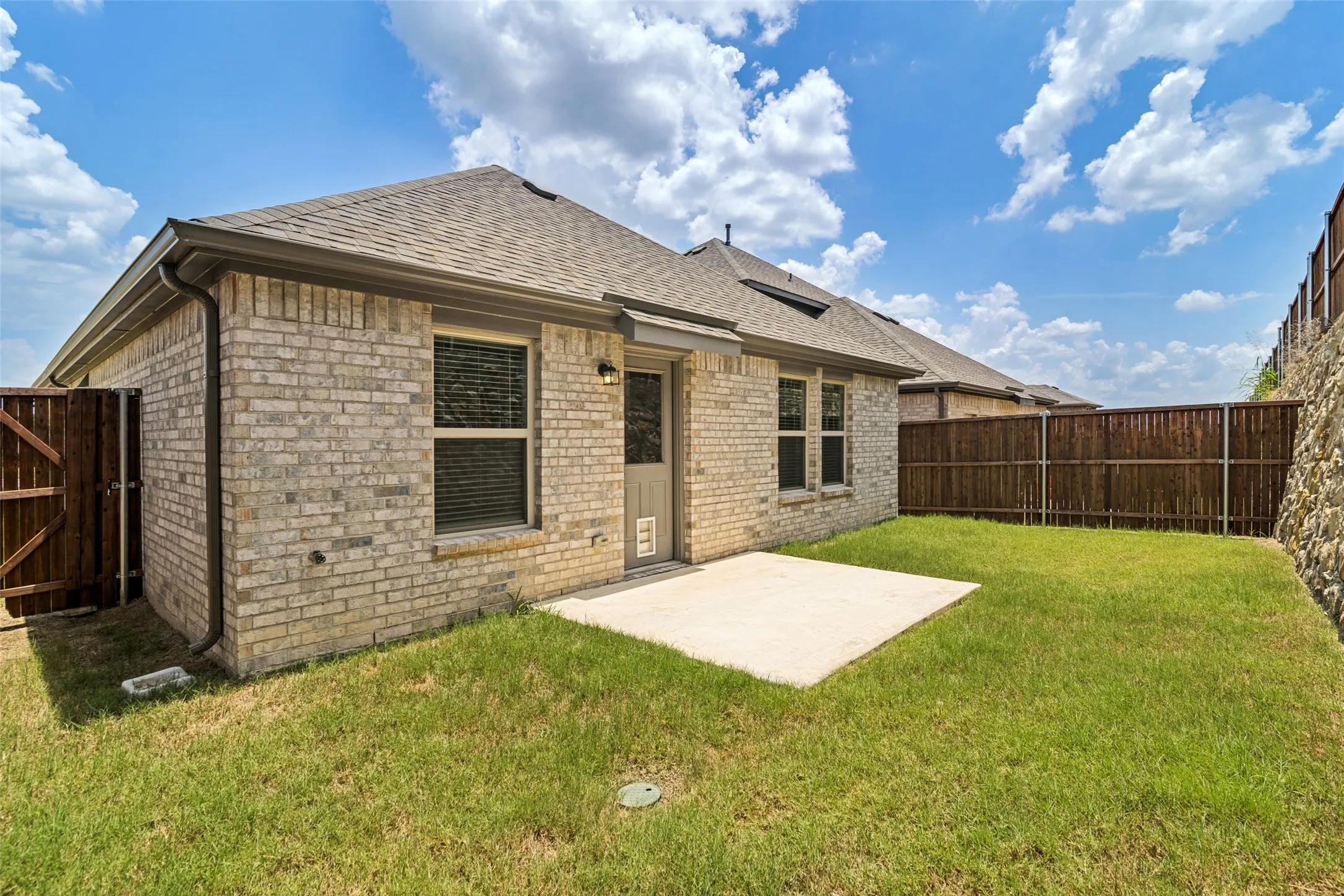 Private backyard with a concrete patio, light-colored brick exterior, and a wooden privacy fence