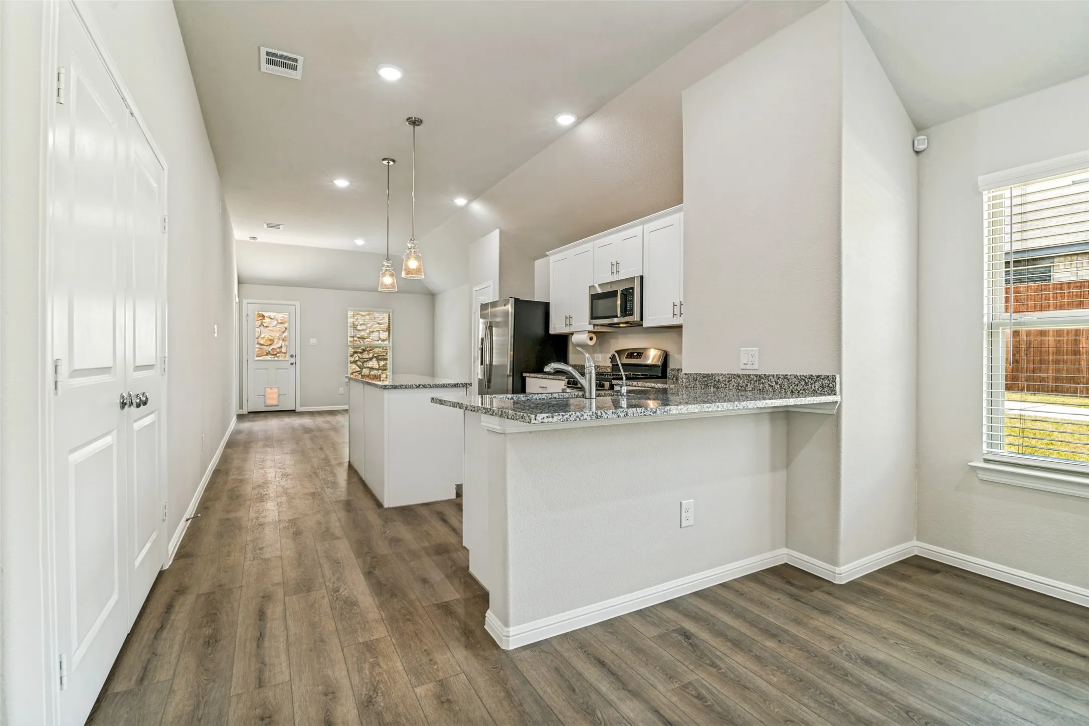 Open-concept kitchen and living area featuring wood-finish flooring, recessed lighting, and a kitchen island with pendant lights