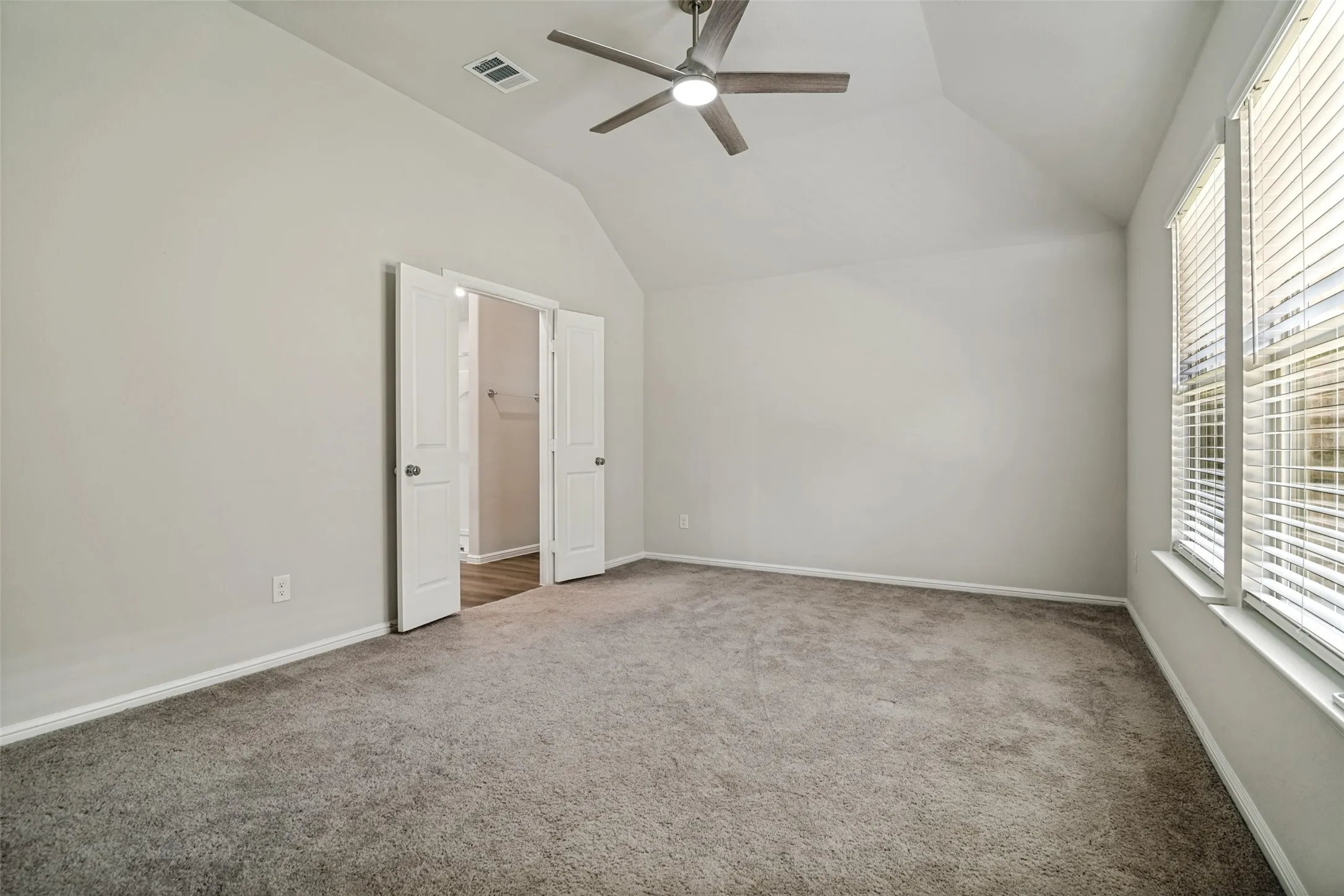 Spacious room featuring vaulted ceilings, a ceiling fan with integrated lighting, and carpet flooring