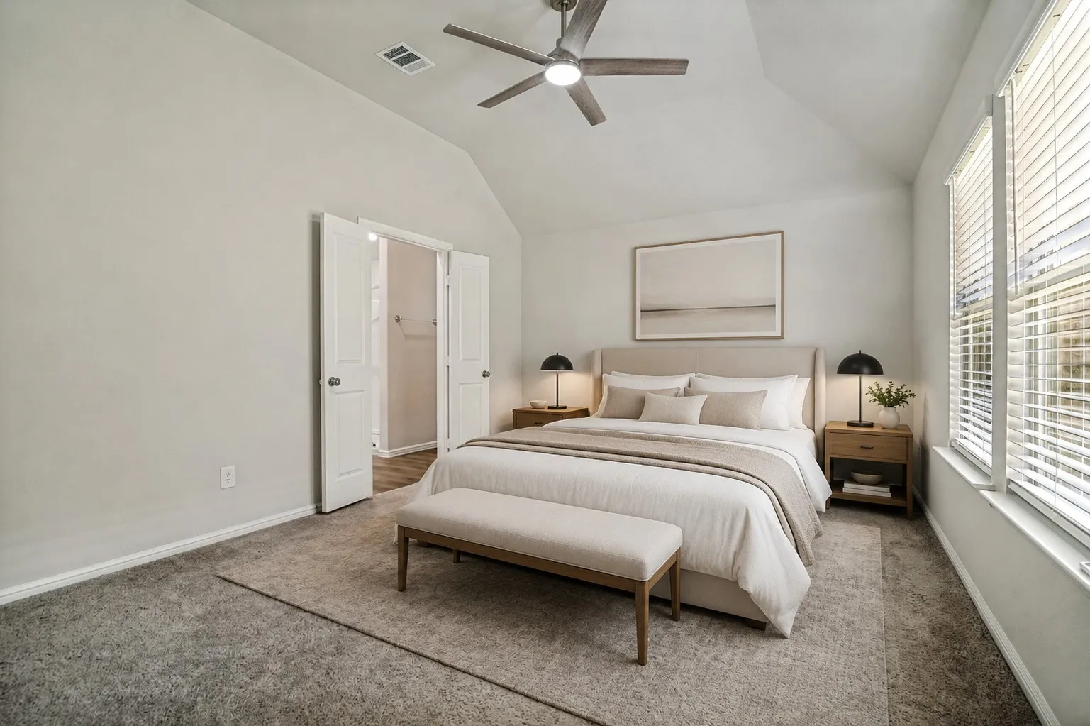 Spacious primary bedroom with vaulted ceilings, ceiling fan with integrated lighting, and abundant natural light from large windows with plantation shutters