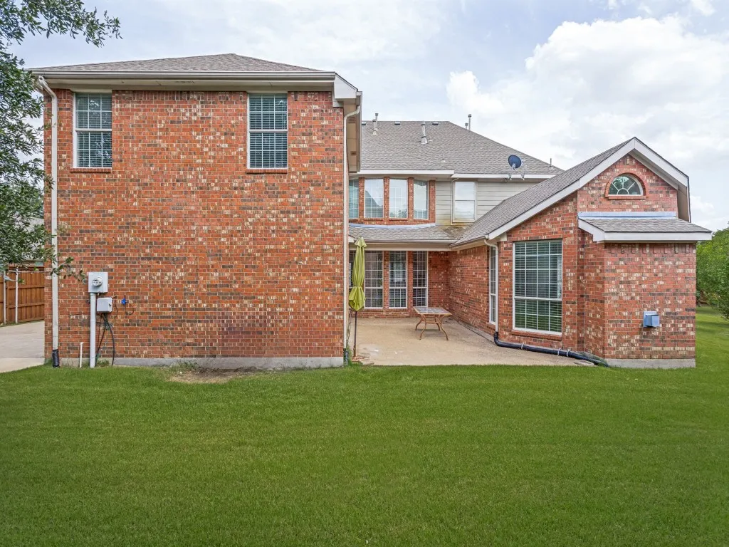 Expansive backyard featuring a lush lawn, a full brick exterior, a paved patio, and multiple large windows with grid patterns