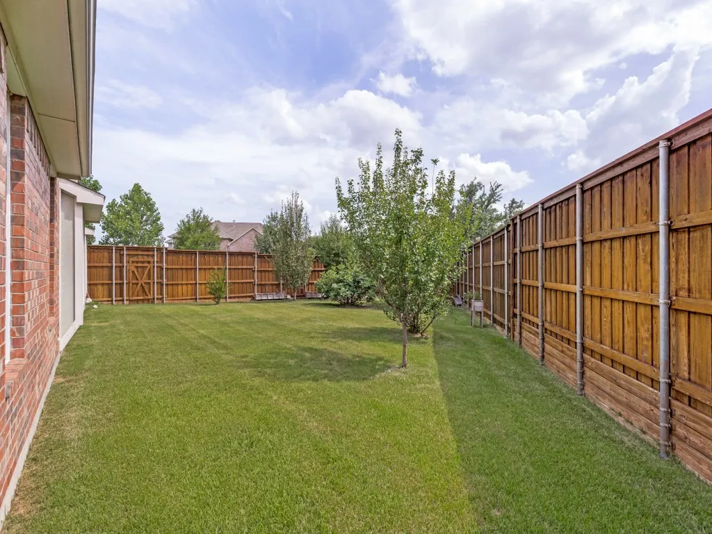 Spacious grassy yard featuring mature trees and full privacy fencing