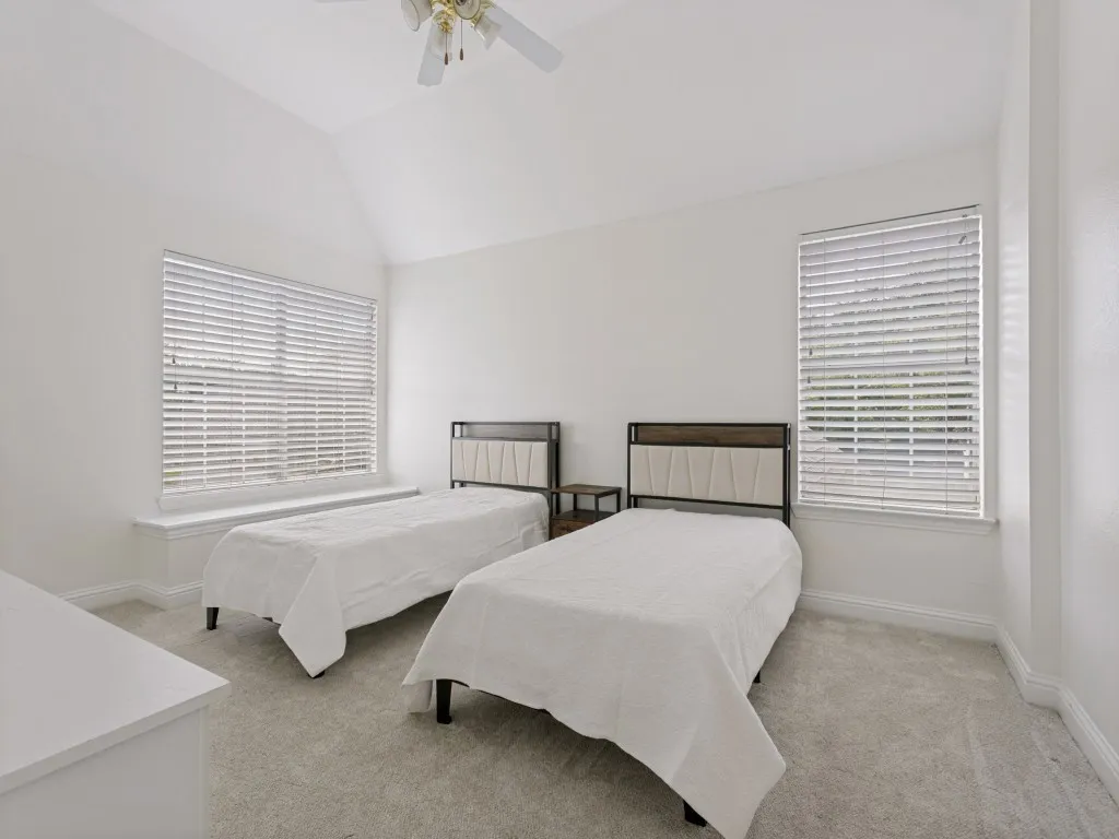 Bedroom featuring vaulted ceilings, light-colored carpeting, two large windows with blinds, and a ceiling fan