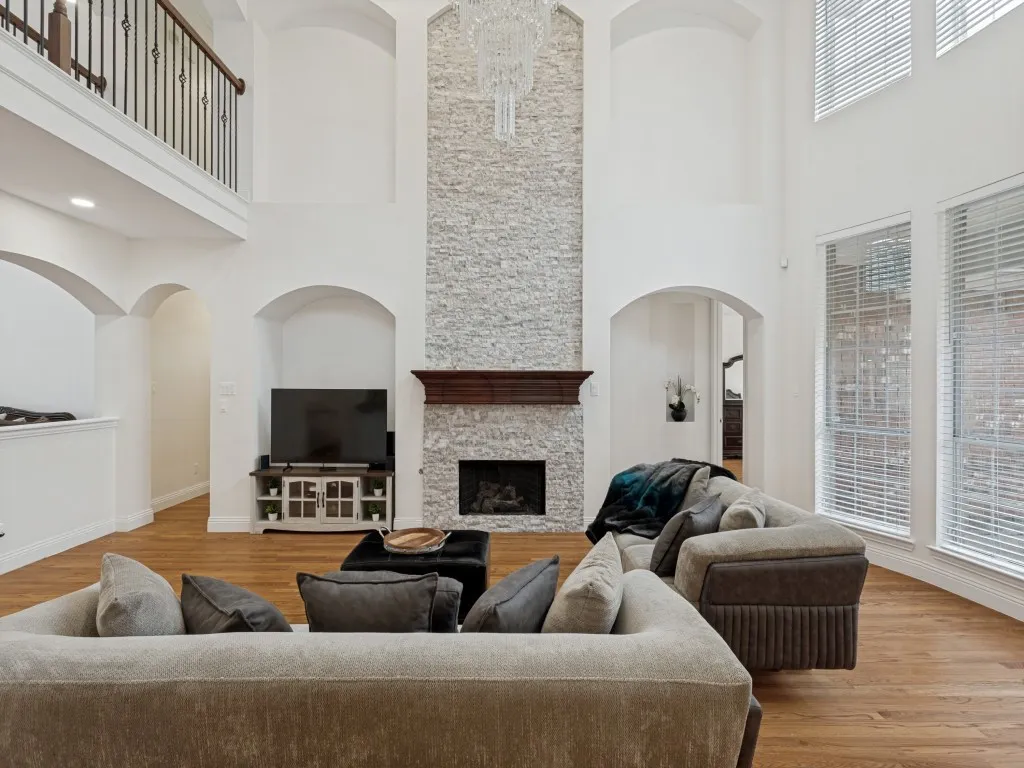 Two-story living area featuring a stacked stone fireplace with a dark wood mantel, high ceilings, wood-finish flooring, and arched doorways