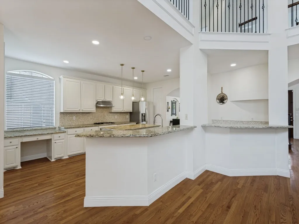 Kitchen featuring extensive cabinetry, stone countertops, a tiled backsplash, and wood-finish flooring