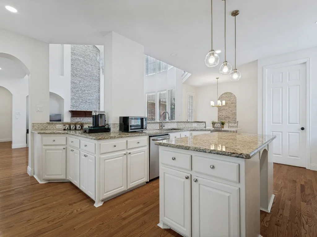 Well-appointed kitchen featuring white cabinetry, granite countertops, a central island, and wood-finish flooring