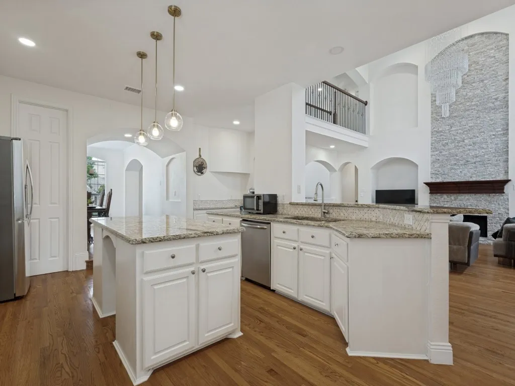 Open-concept kitchen featuring an island, granite countertops, wood-finish flooring, white cabinetry, and stainless steel appliances