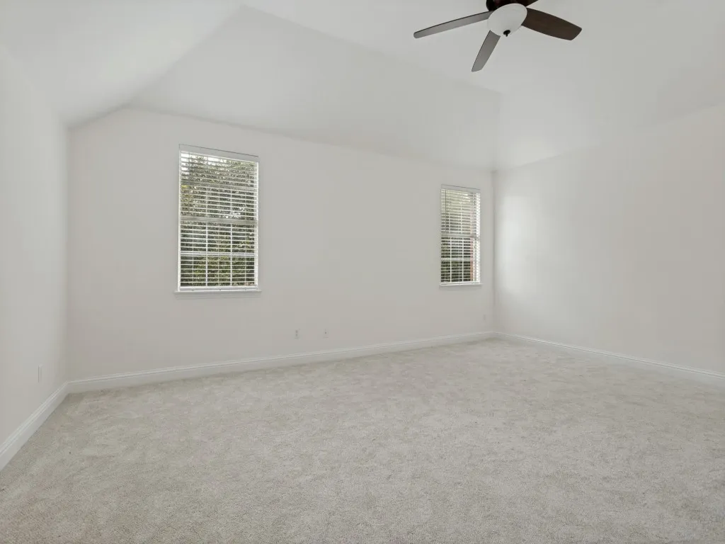 Spacious room featuring vaulted ceilings, light-colored carpeting, and a ceiling fan