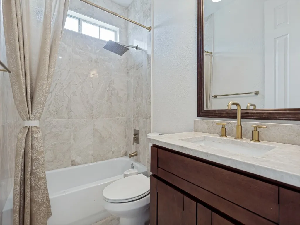 Bathroom featuring a single vanity with a stone countertop and gold-finish faucet, a white undermount sink, and a framed mirror