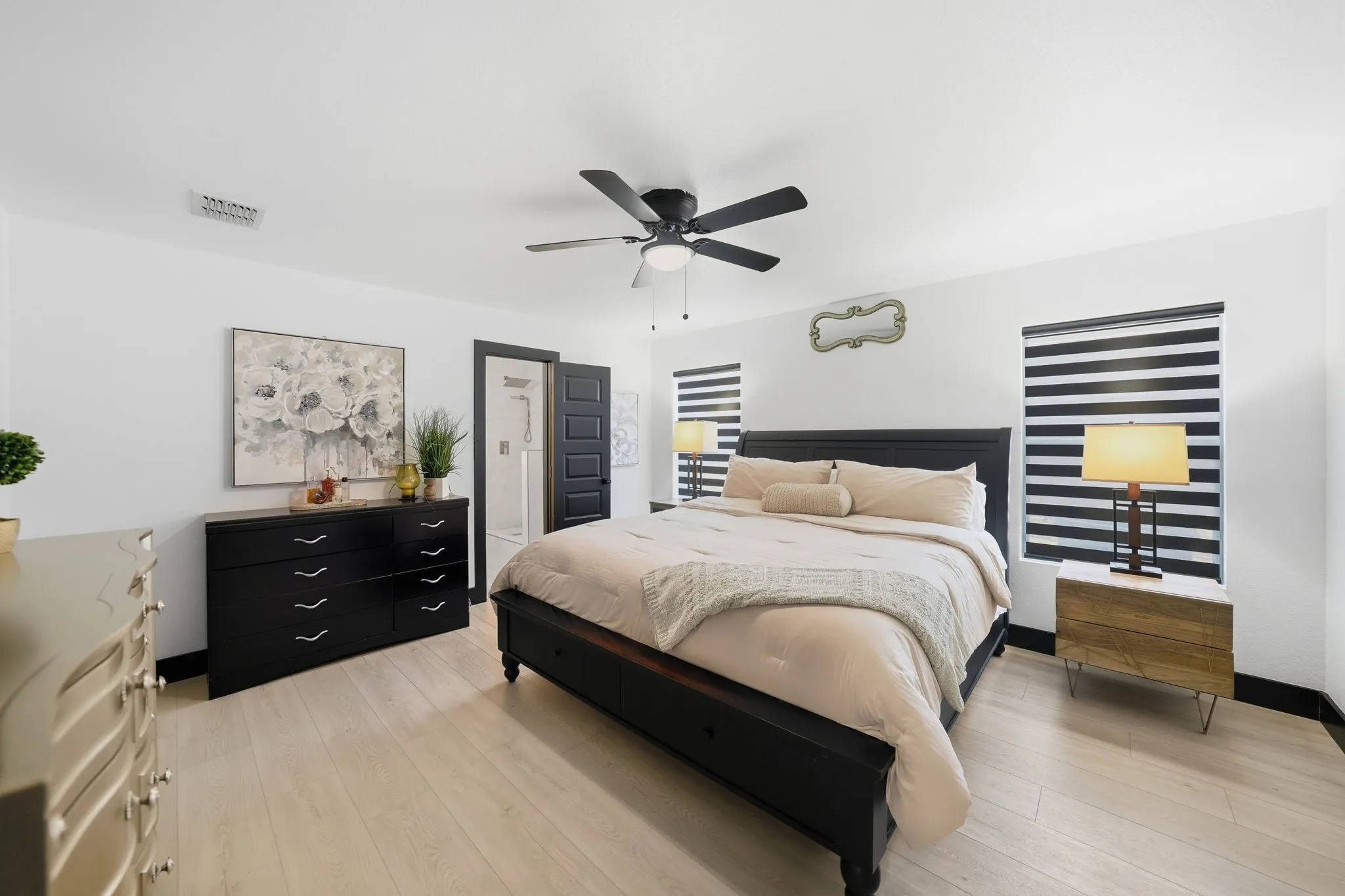 Spacious room featuring light wood-finish flooring, a ceiling fan, dual windows with banded blinds, and a dark trim package