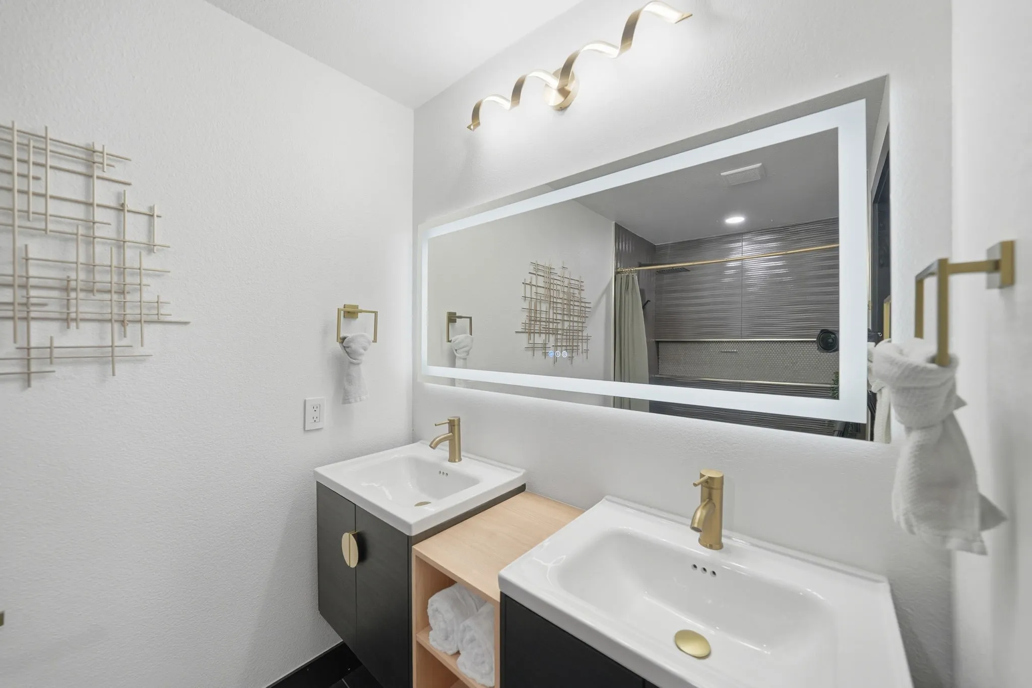 Dual floating vanities featuring matte black cabinetry with gold hardware, integrated white sinks, and gold-finish faucets