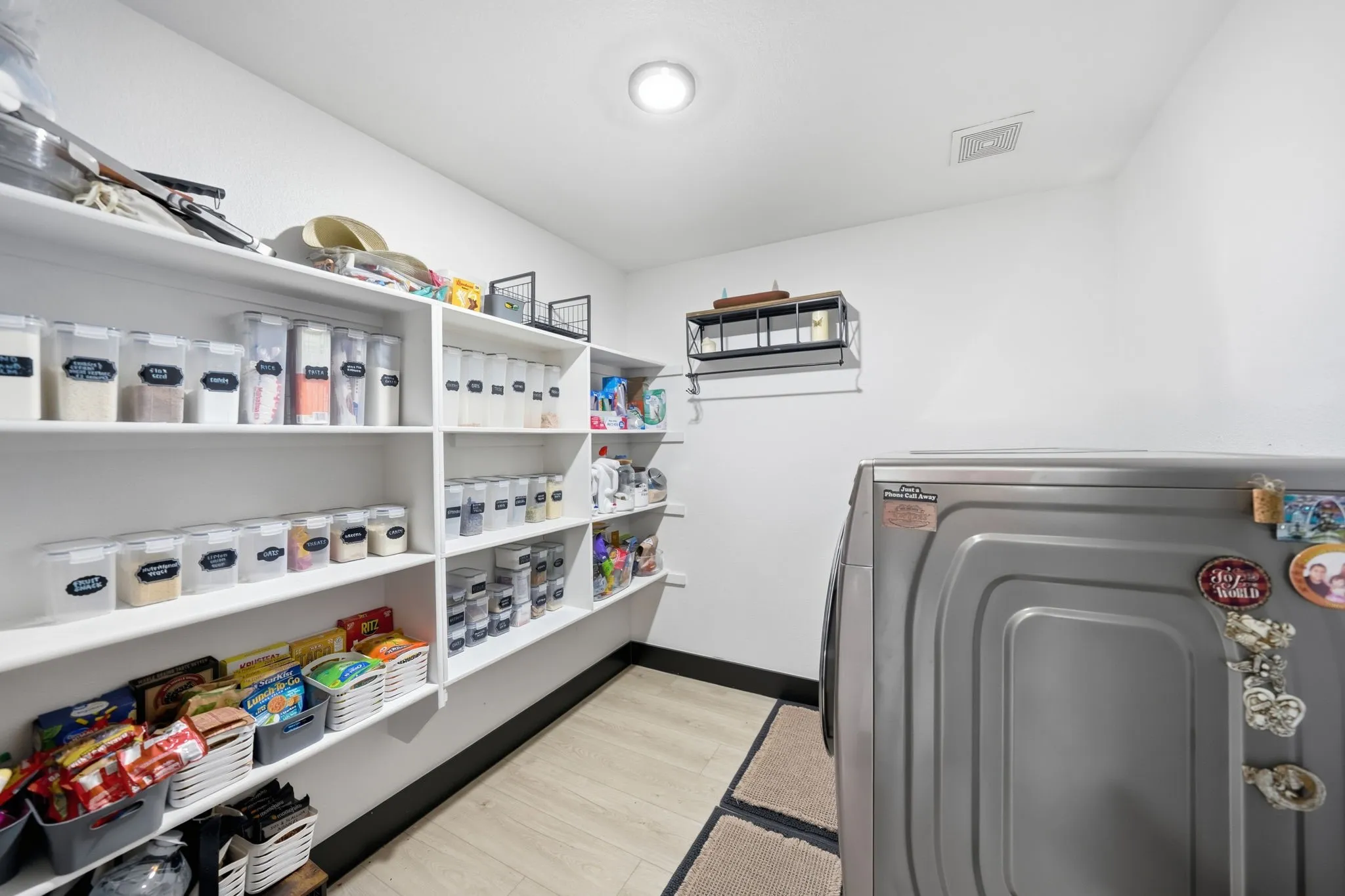 Spacious utility room featuring extensive built-in shelving, recessed ceiling lighting, and light wood-finish flooring
