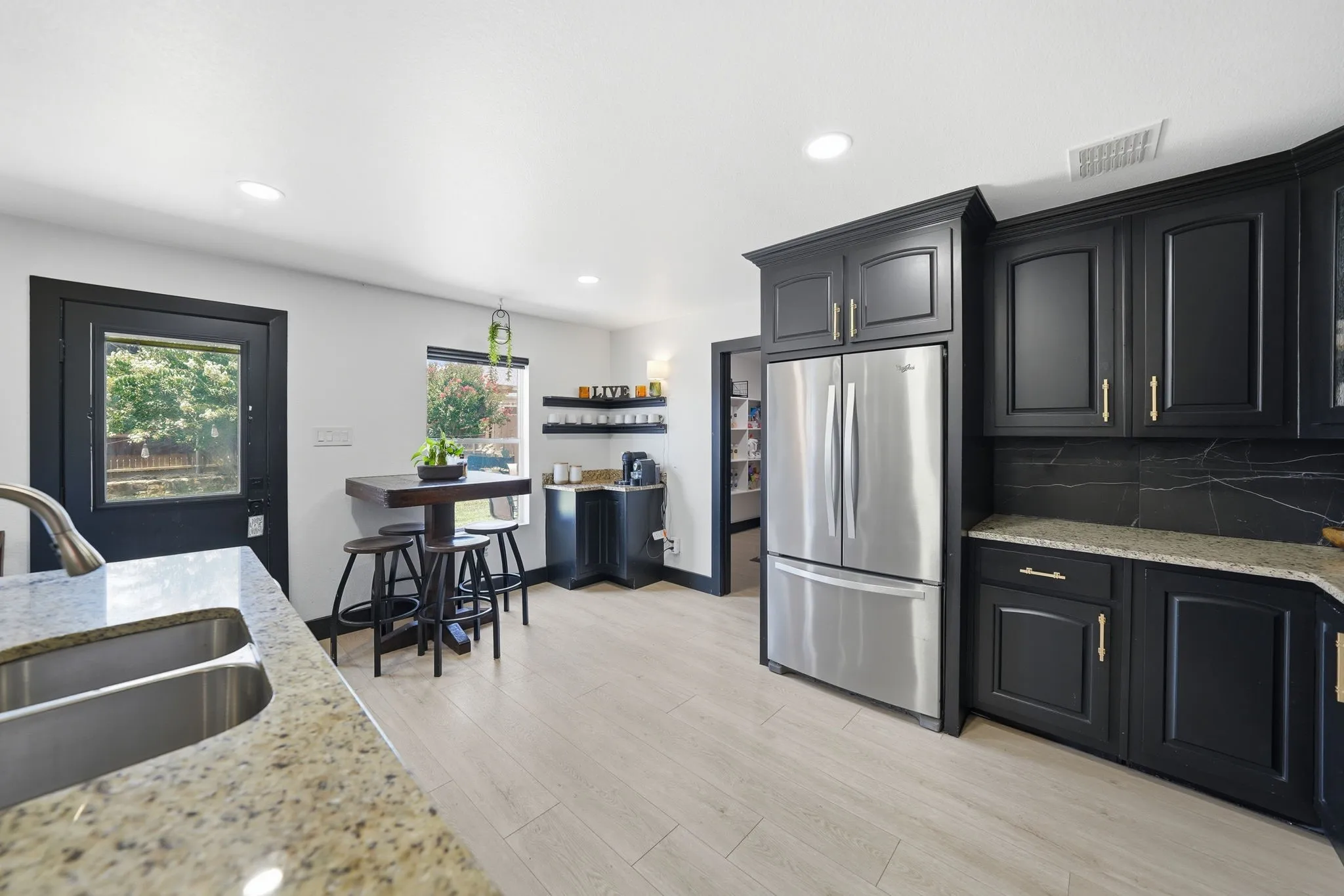 Modern kitchen featuring black cabinetry, light wood-finish flooring, a stainless steel refrigerator, granite countertops, and a black slab backsplash