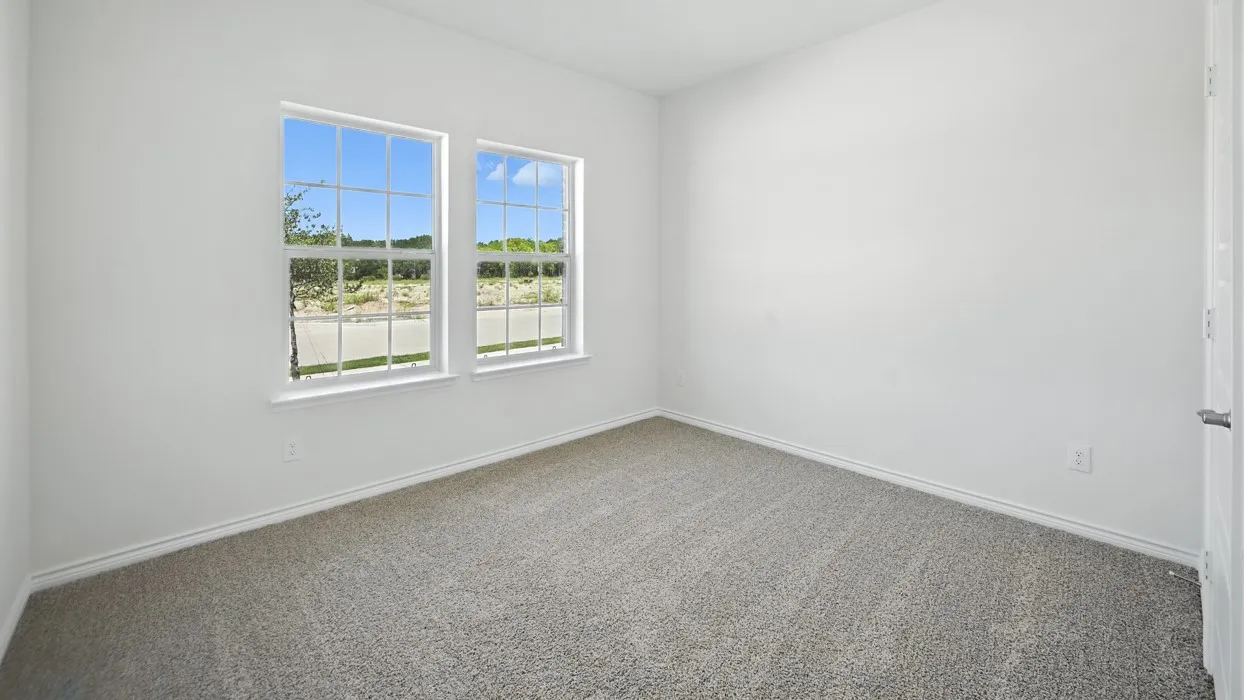Bright interior space featuring two large windows with grid panes, neutral gray carpet, white walls, white baseboards, and a white interior door with a brushed nickel handle