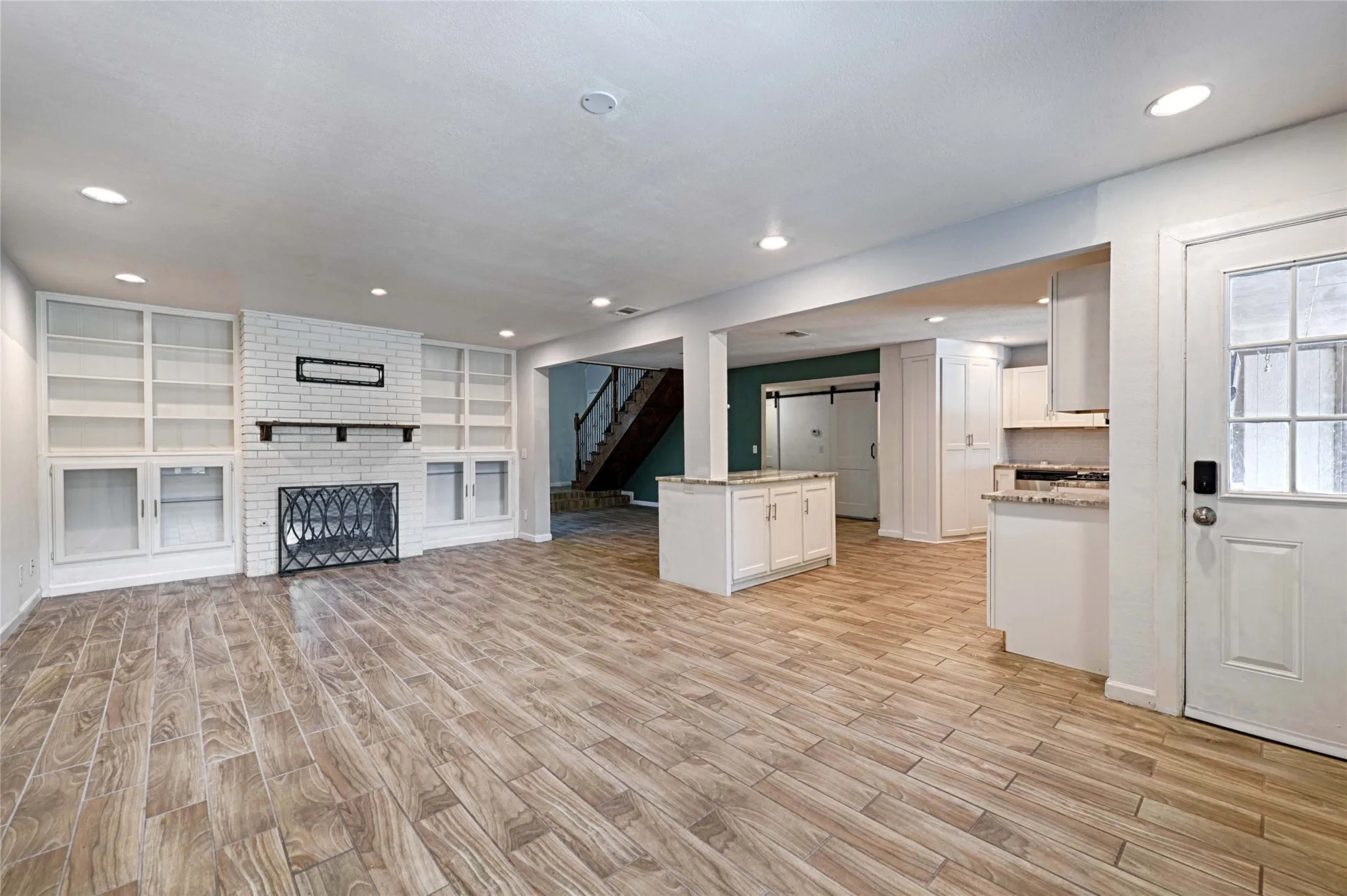 Expansive living area featuring wood-finish flooring, a white brick fireplace with a mantel, and built-in shelving with lower cabinetry