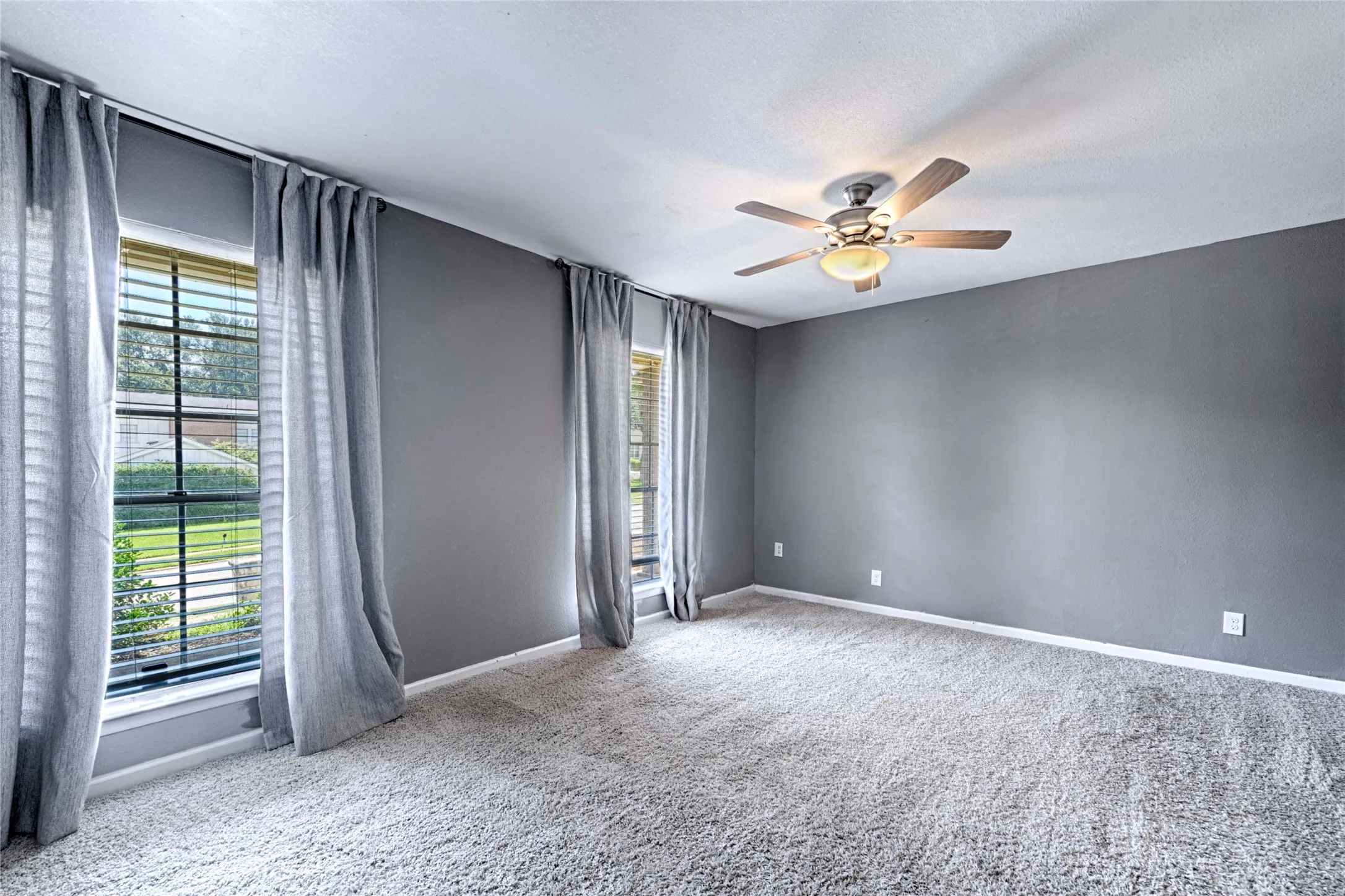 Spacious room featuring light gray carpeting, neutral wall finishes, and a ceiling fan with integrated lighting