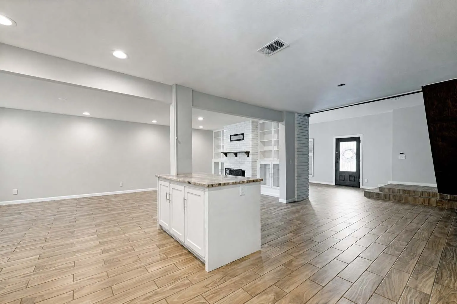 Open-concept living space featuring wood-look tile flooring, recessed lighting, and a kitchen island with a stone countertop
