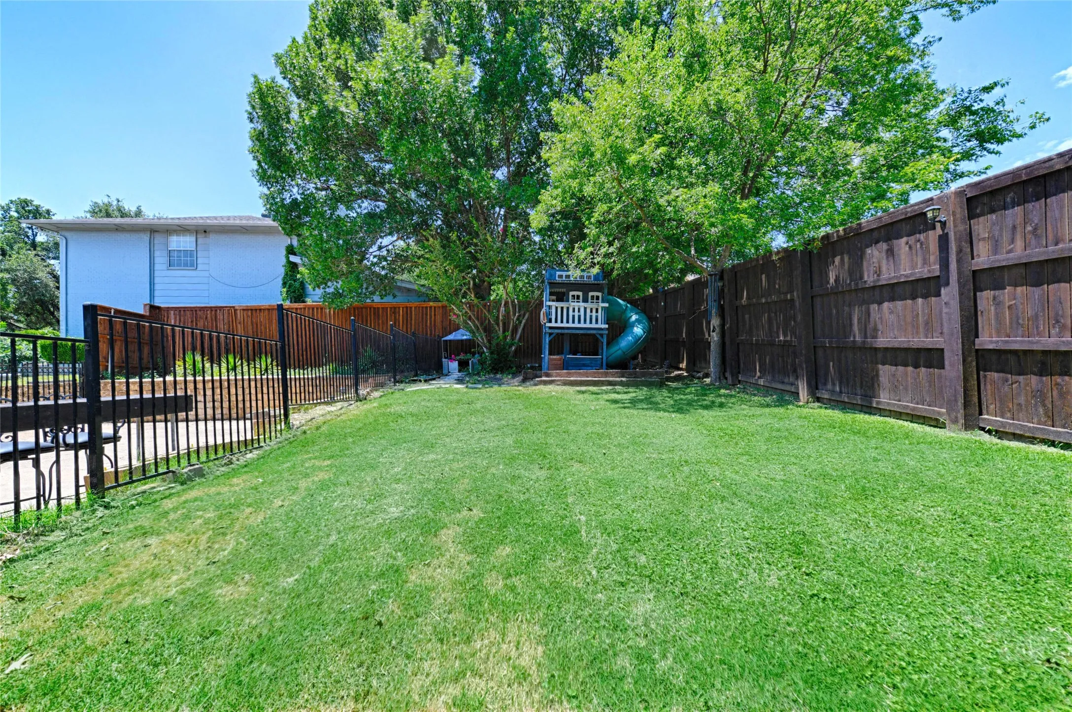Expansive backyard featuring a large grassy area, a dark wood privacy fence, a black metal fence, and mature trees providing natural shade