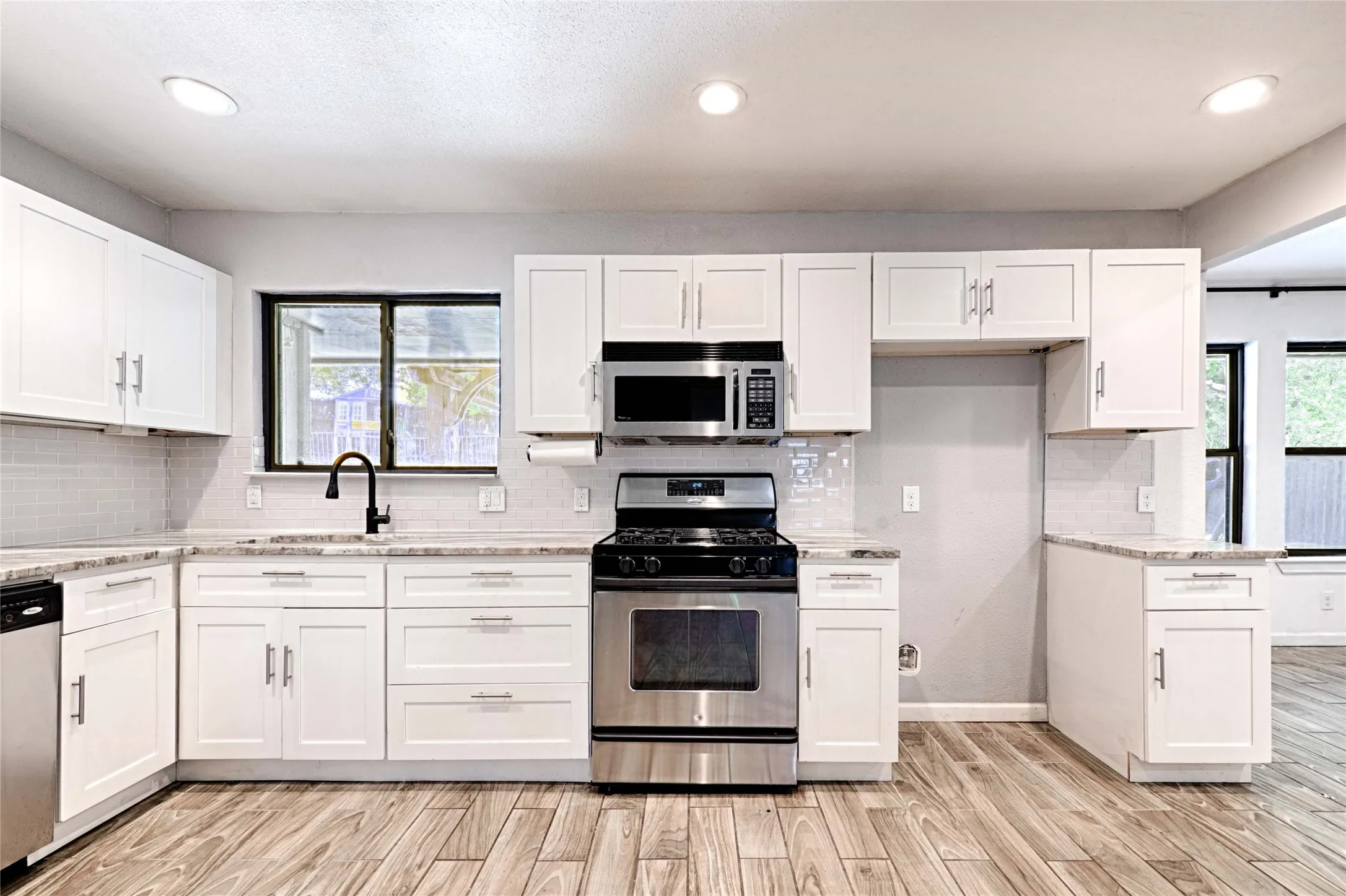 Modern kitchen featuring white shaker cabinetry with brushed nickel hardware, light-toned countertops, a stainless steel gas range, and wood-finish flooring