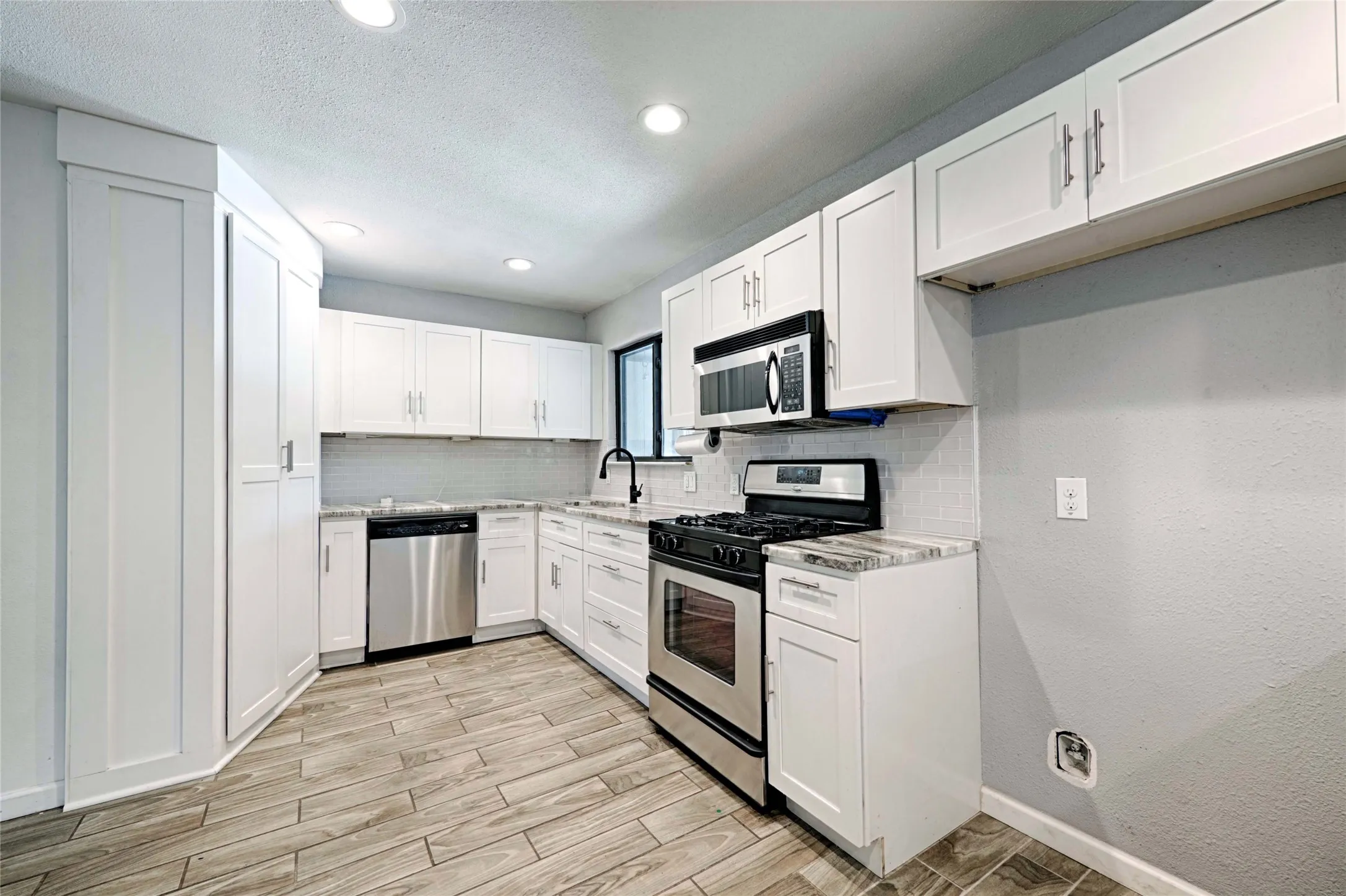 Kitchen featuring wood-finish flooring, white cabinetry, stainless steel appliances, speckled countertops, and a white subway tile backsplash