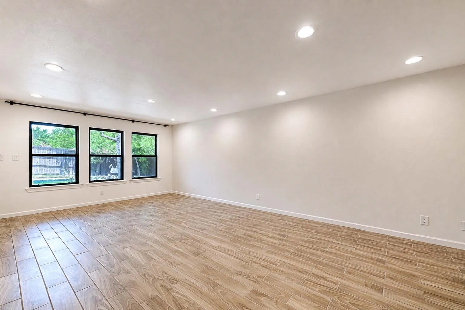 Bright interior space featuring wood-finish tile flooring, recessed ceiling lighting, and multiple windows with black trim