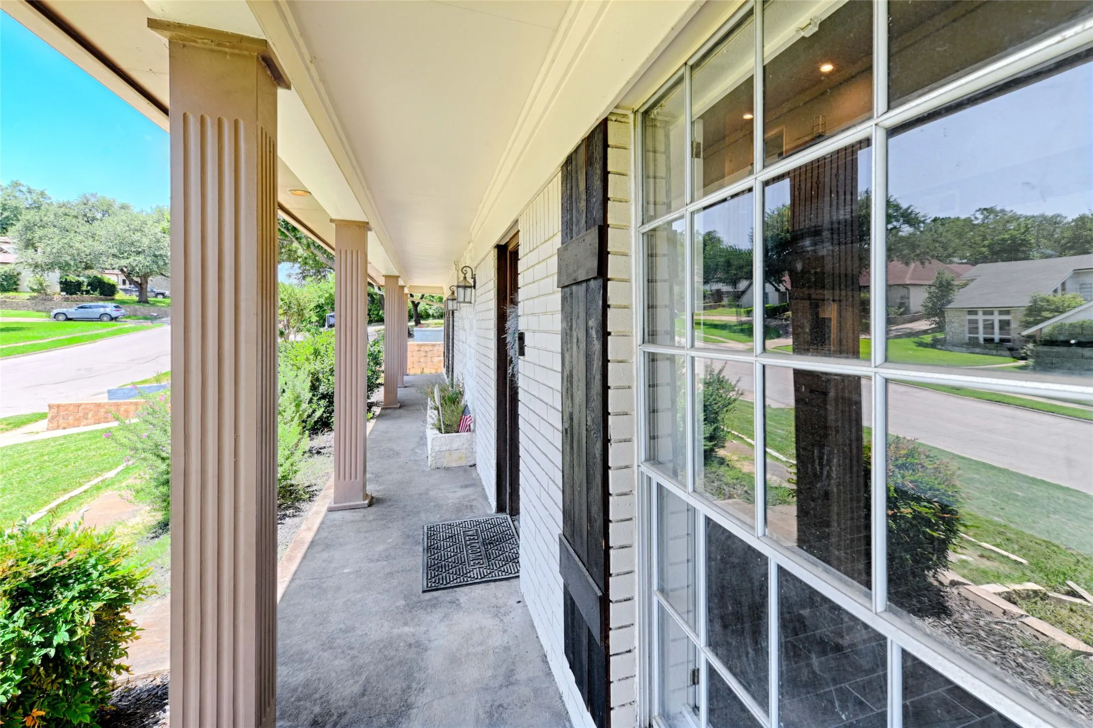 Expansive covered porch featuring fluted columns and a white brick facade