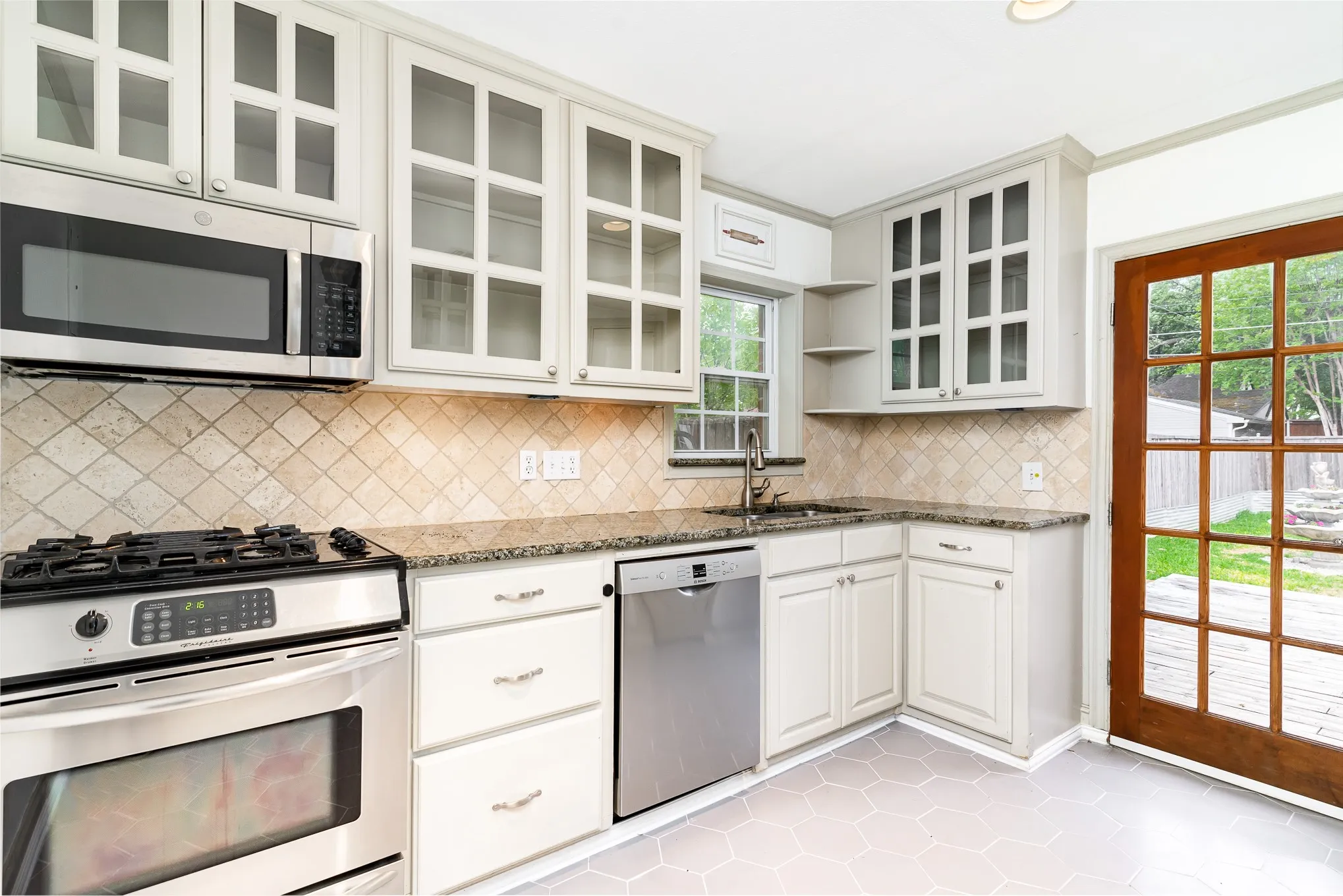 Kitchen with stainless steel appliances, open shelves, a sink, stone counters, and tasteful backsplash