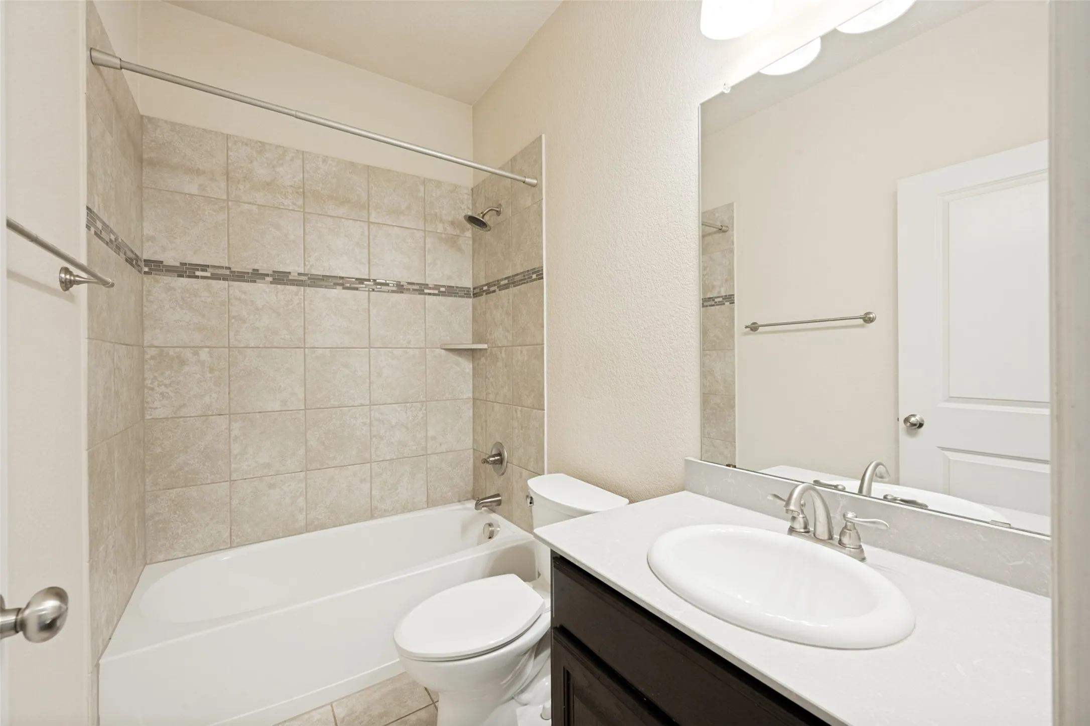 Bathroom with a built-in tub and shower combination featuring neutral-toned tile surround with a decorative accent band