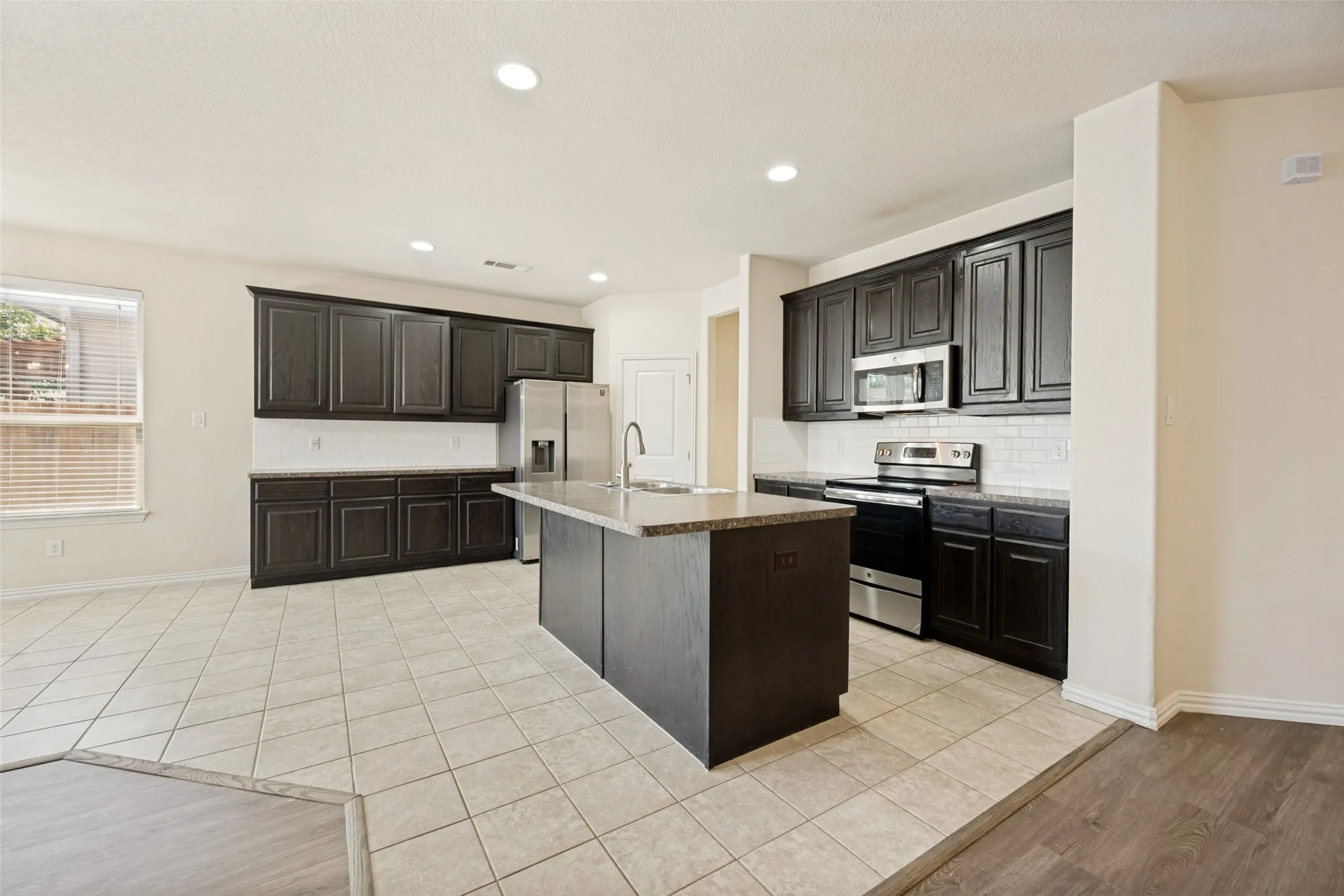Kitchen featuring dark wood cabinetry, a central island with a sink, stainless steel appliances, and light tile flooring