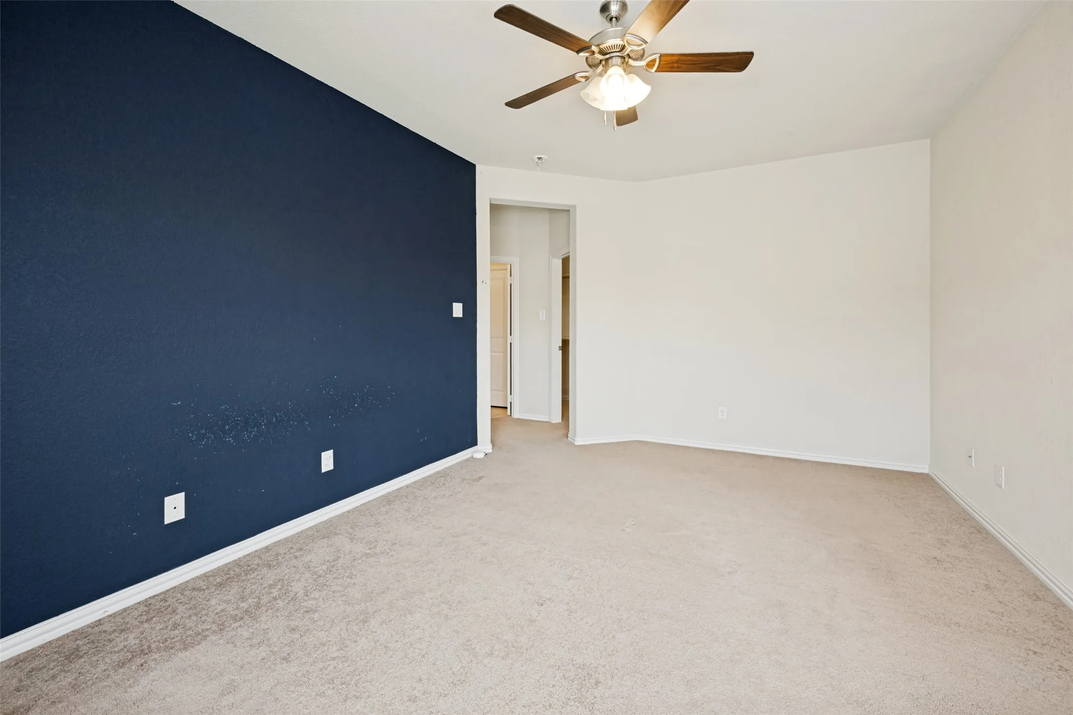 Spacious room featuring a dark accent wall, light neutral carpeting, and a ceiling fan with integrated lighting