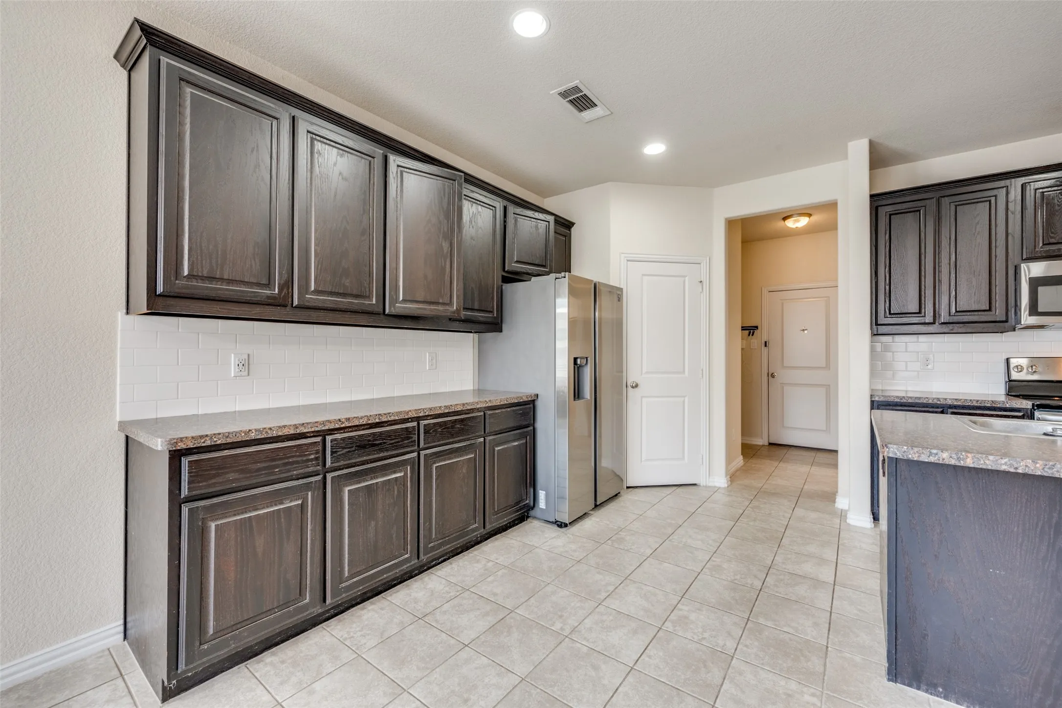 Kitchen featuring dark wood-finish cabinetry, light-toned countertops, subway tile backsplash, and tile flooring