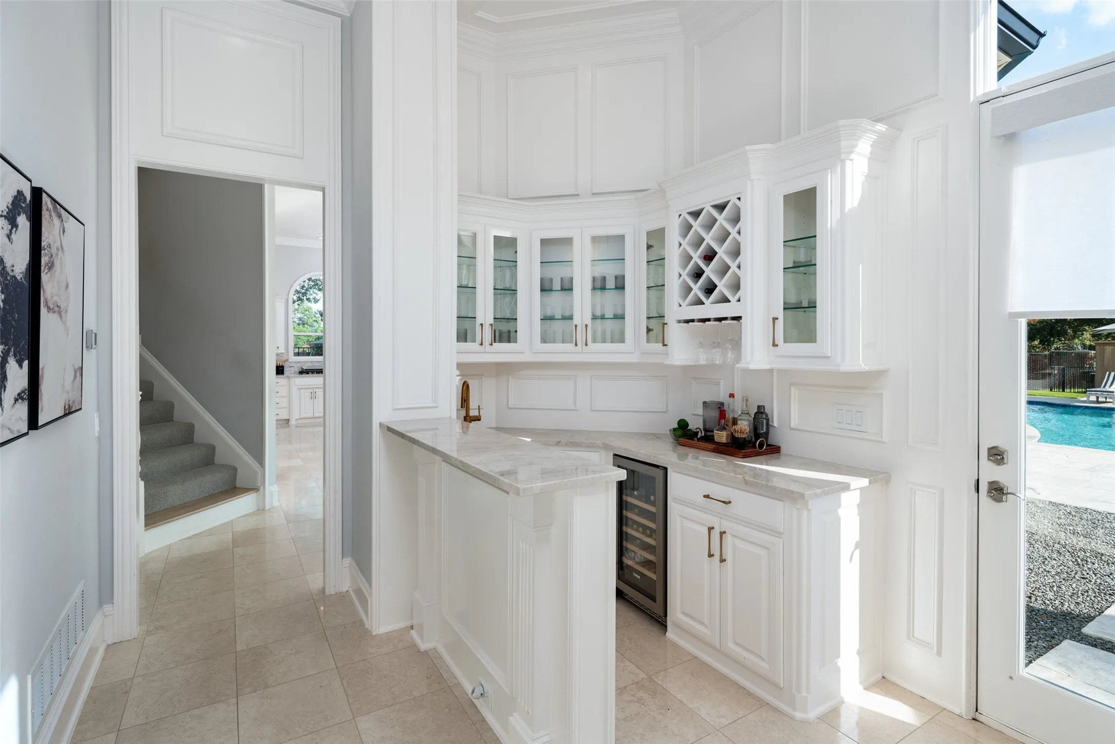 The elegant wet bar offers a wine refrigerator, sink, glass-front cabinetry, display shelving, and serving space, creating the perfect transition between indoor entertaining and the outdoor living areas