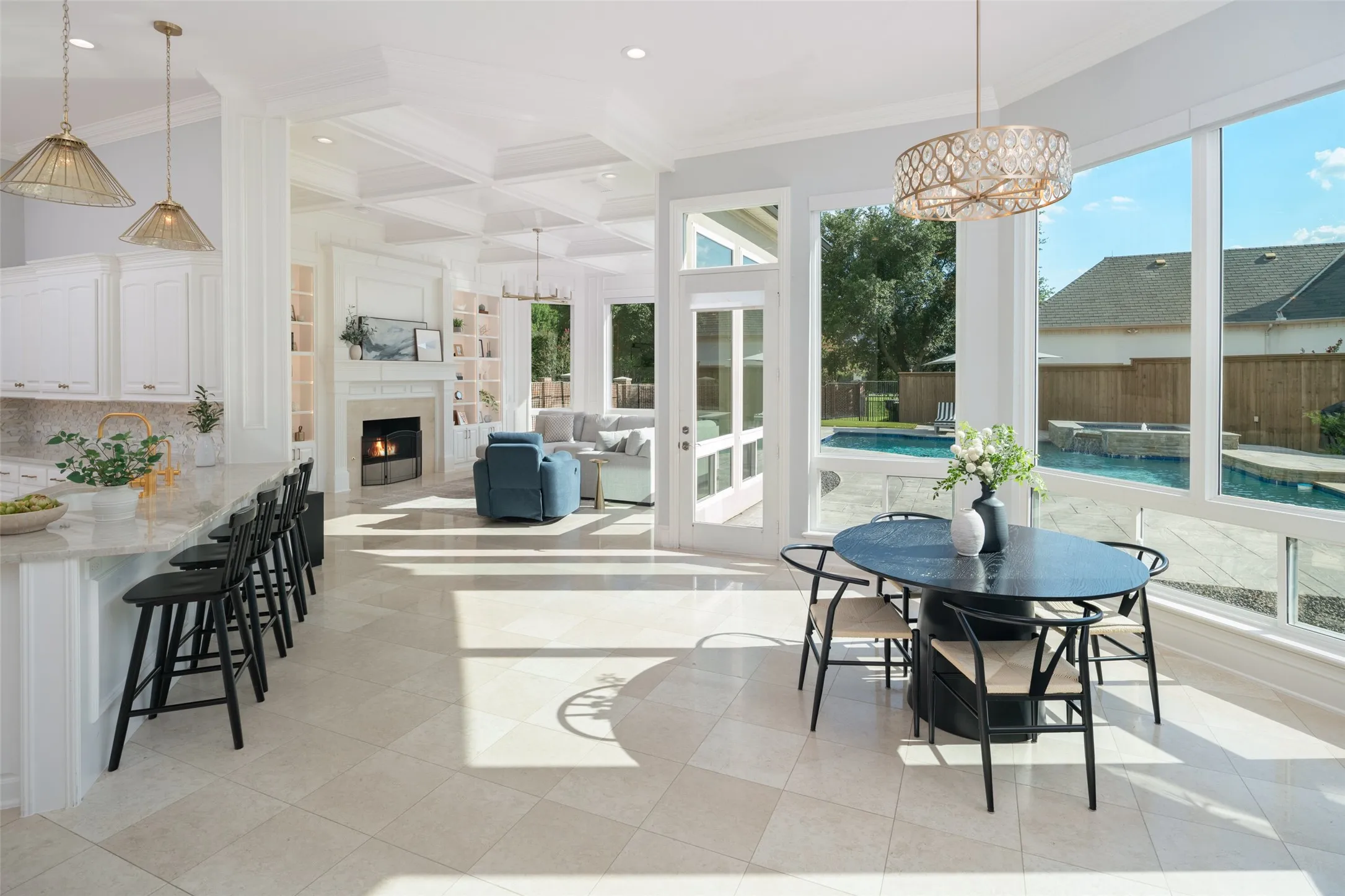 Expansive open-concept living, dining, and kitchen spaces are connected by soaring ceilings, a dramatic coffered ceiling, abundant natural light, and walls of windows overlooking the resort-style backyard and pool.