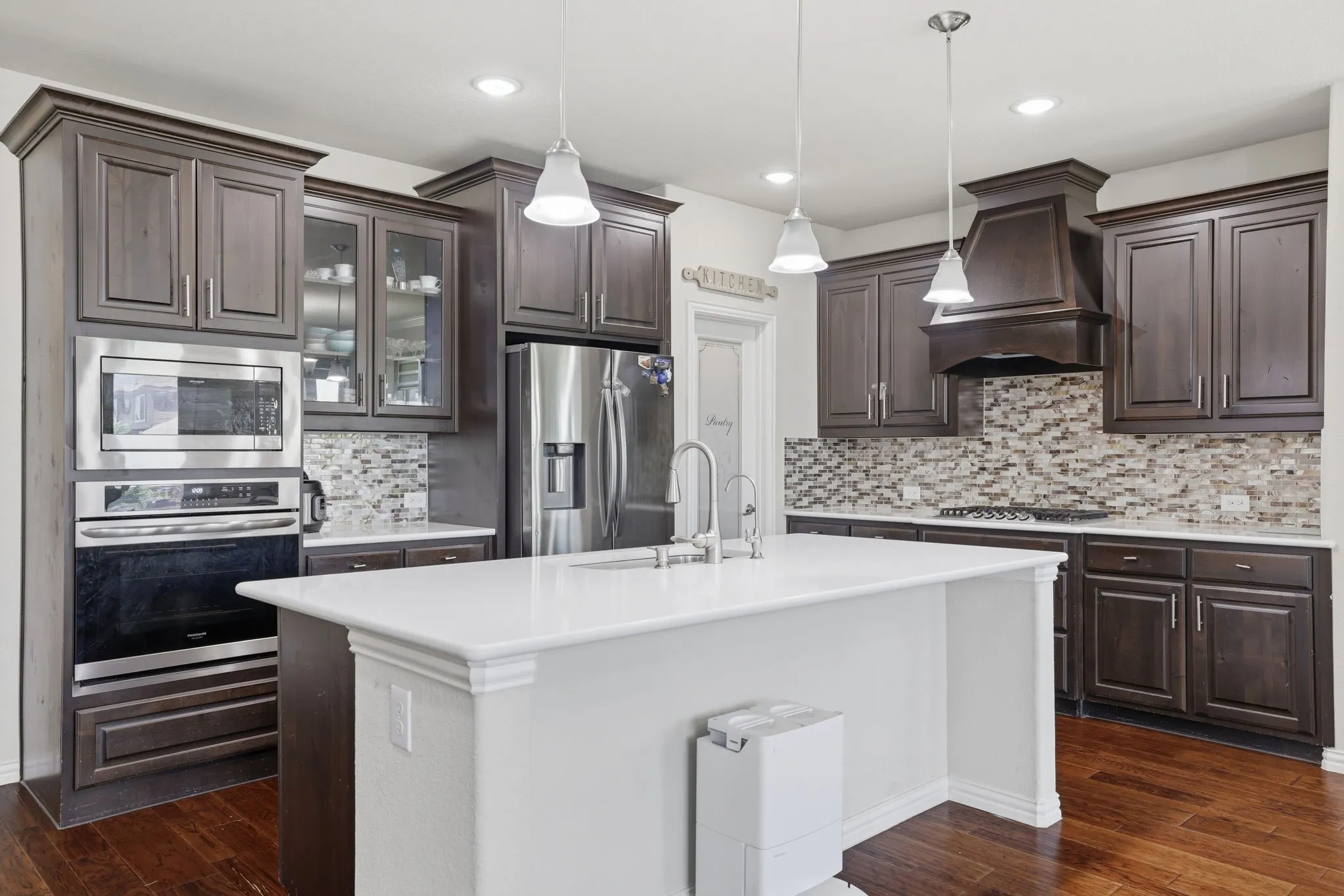 Kitchen featuring a central island with white countertop, dark wood-finish cabinetry, stainless steel appliances, and a mosaic tile backsplash