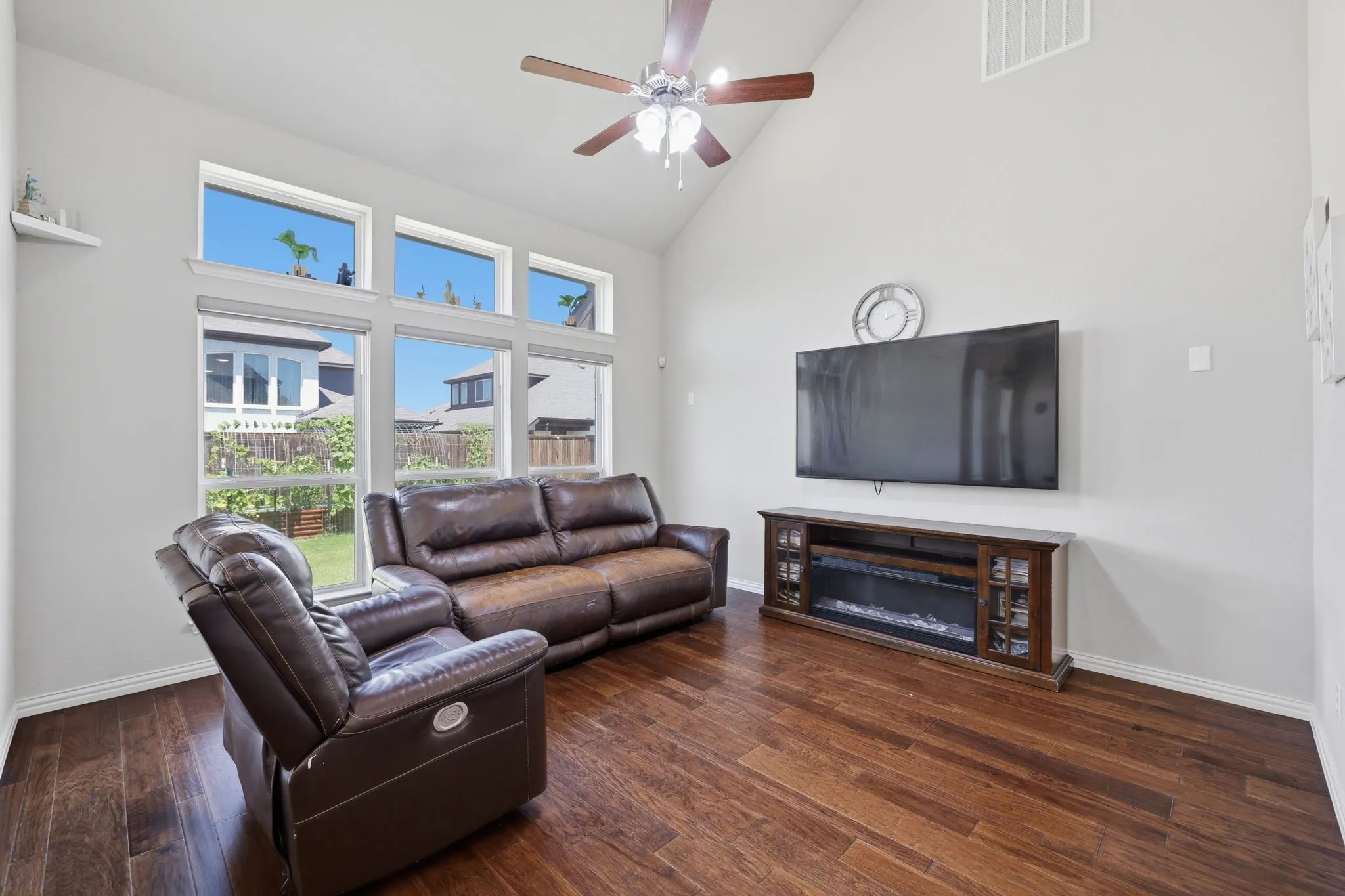 Vaulted ceiling with a ceiling fan, wood-finish flooring, and a wall of windows featuring transom windows