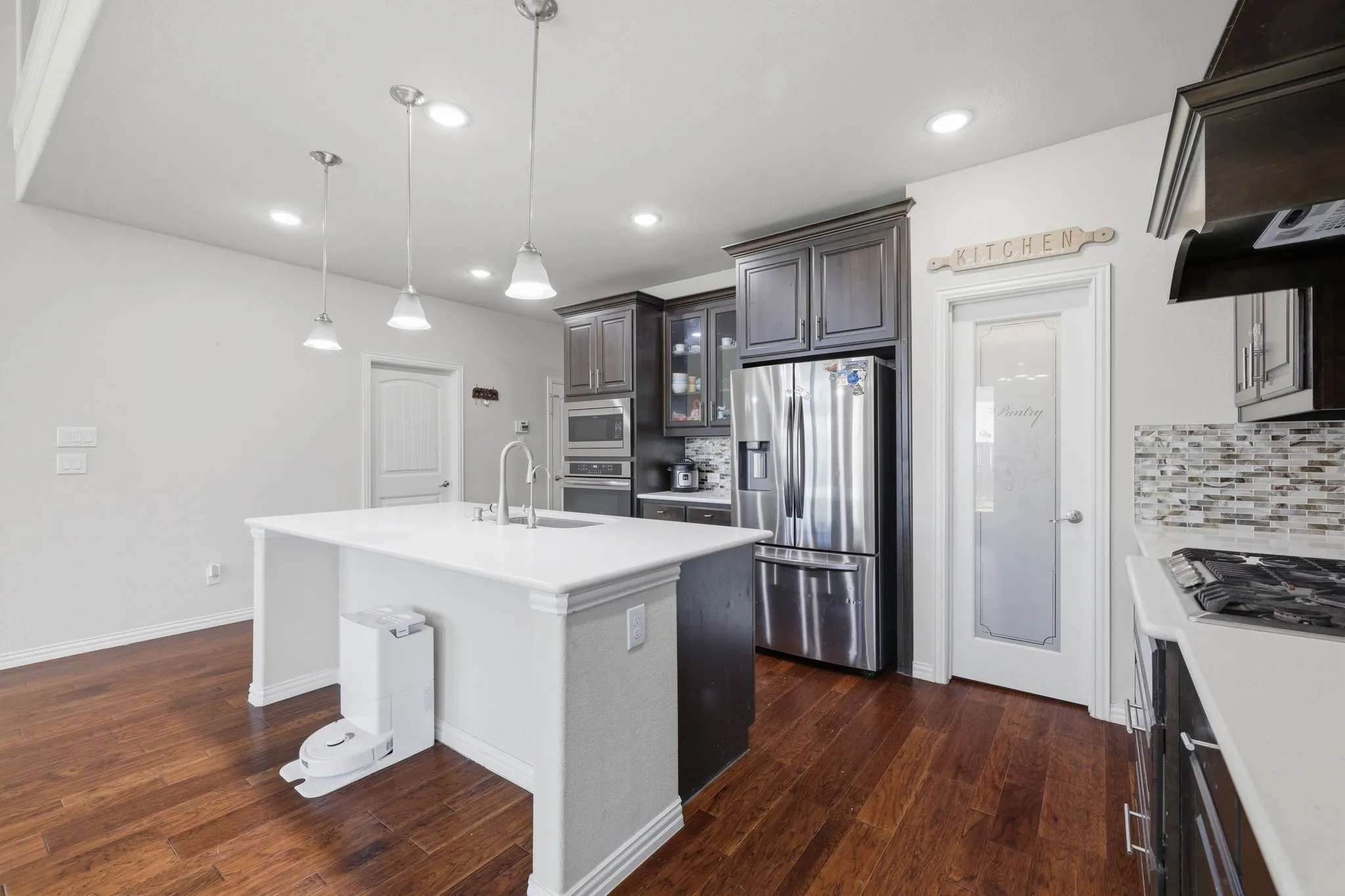 Kitchen featuring a central island with a sink, white countertops, dark wood-finish cabinetry, stainless steel appliances, and wood-finish flooring