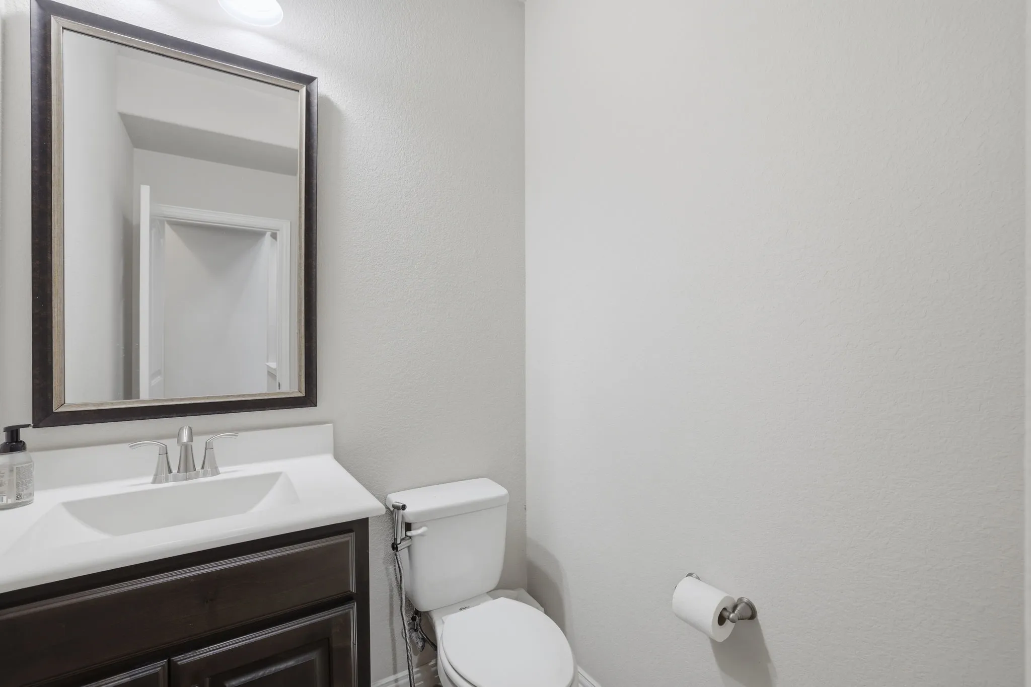 Powder room featuring a framed vanity mirror, built-in vanity with a white countertop and integrated sink, and dark wood-finish cabinetry with silver-tone hardware
