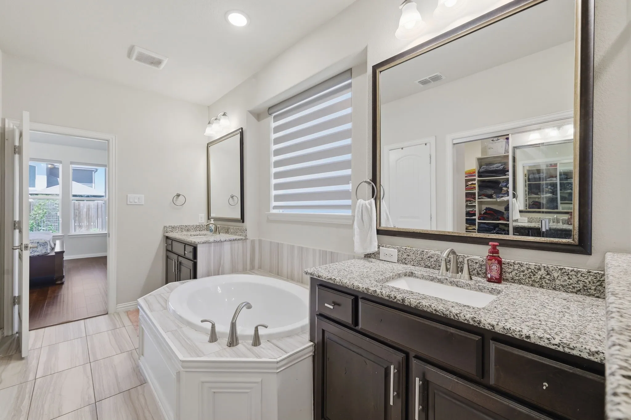 Bathroom featuring a built-in soaking tub, dual vanities with granite countertops, wood-finish cabinetry, and tiled flooring