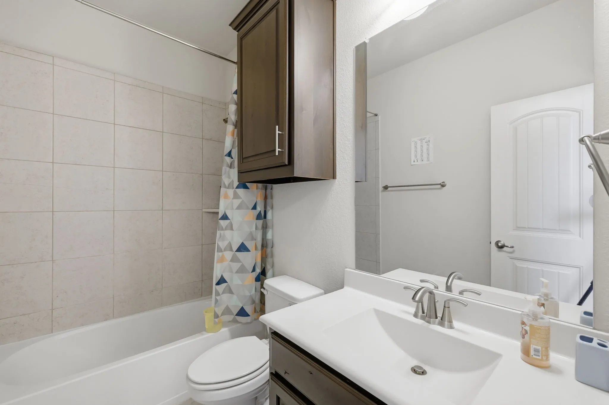 Bathroom featuring a tub/shower combination with light-toned wall tiling, a vanity with an integrated sink, a rectangular mirror, and a dark wood-finish wall cabinet