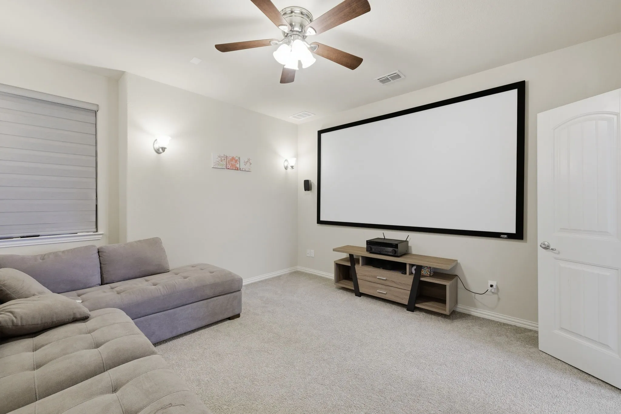 Media room featuring a large projection screen, recessed lighting, and wall-mounted sconces