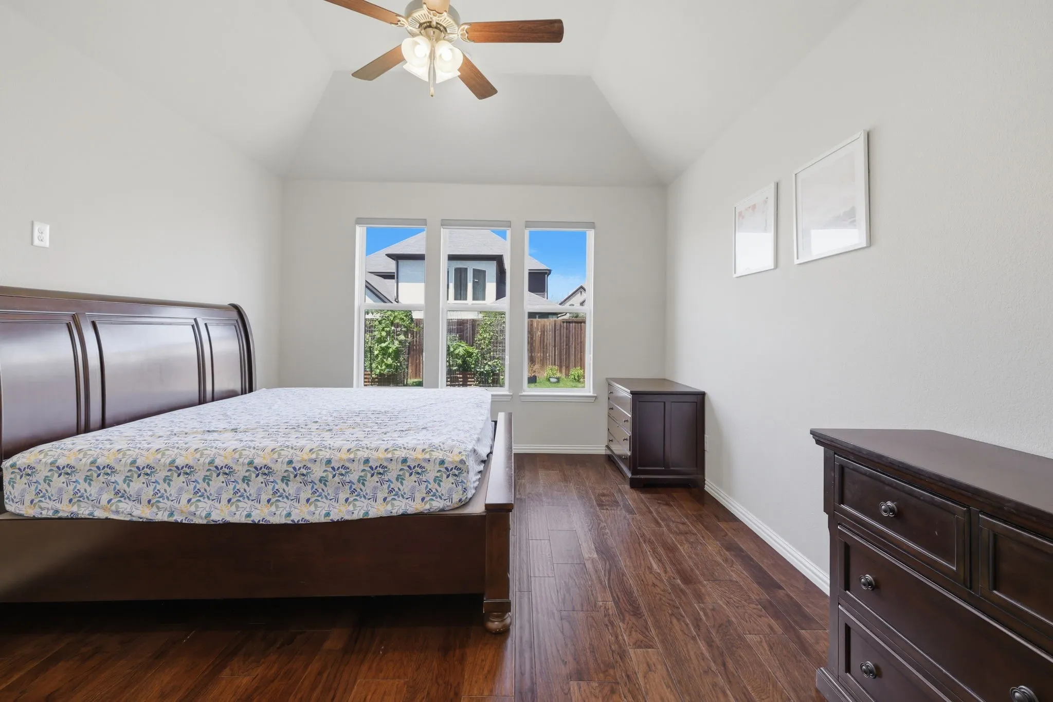 Spacious room featuring vaulted ceilings, wood-finish flooring, a ceiling fan with integrated lighting, and multiple windows providing natural illumination