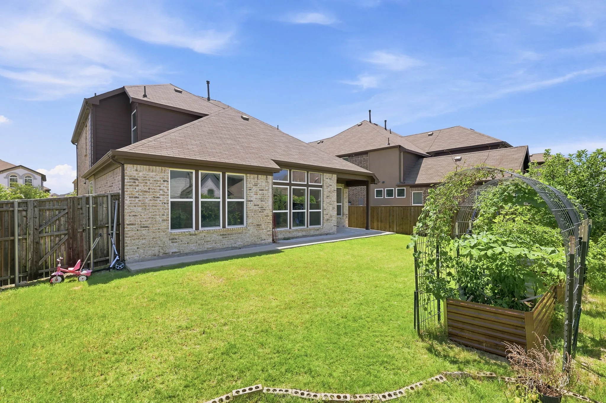 Expansive backyard featuring a manicured lawn, a covered patio, and a raised garden bed with an arched trellis