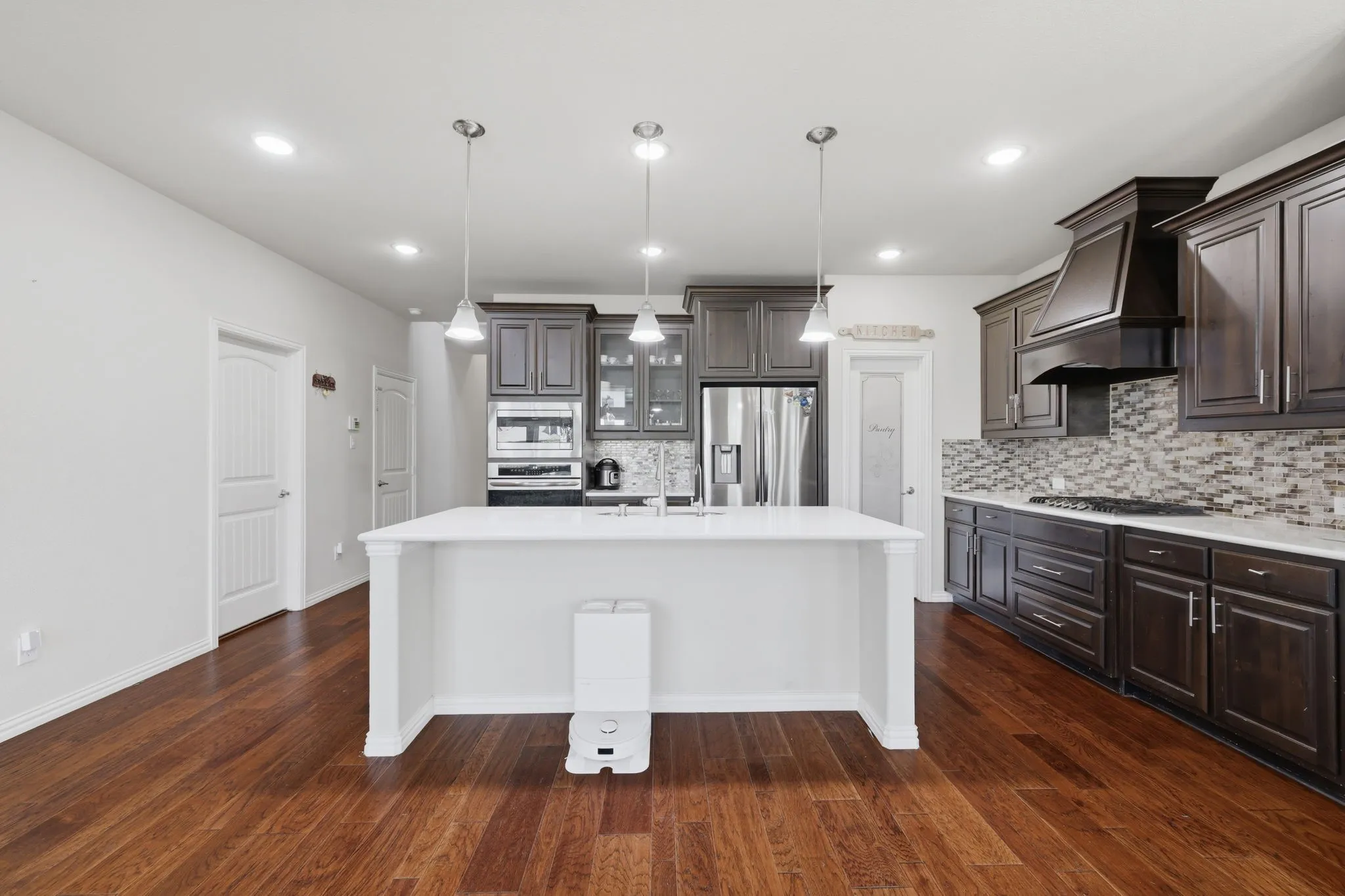 Kitchen featuring a large central island with pendant lighting, dark wood cabinetry, stainless steel appliances, mosaic tile backsplash, and wood-finish flooring